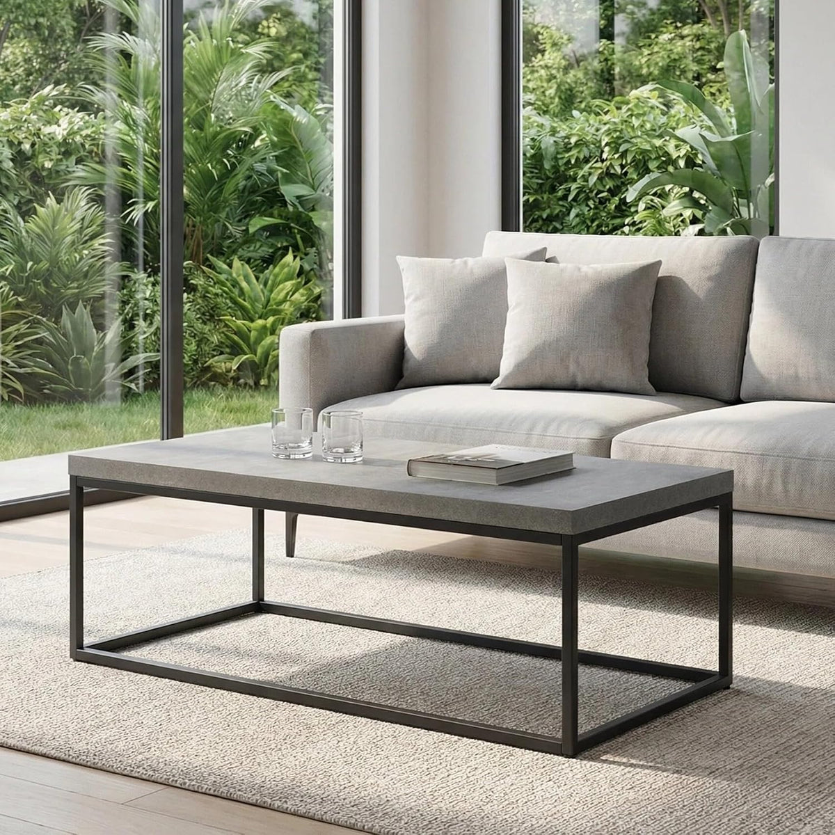 Concrete-look rectangular coffee table with slim black metal frame beside a pale gray sofa and large windows.