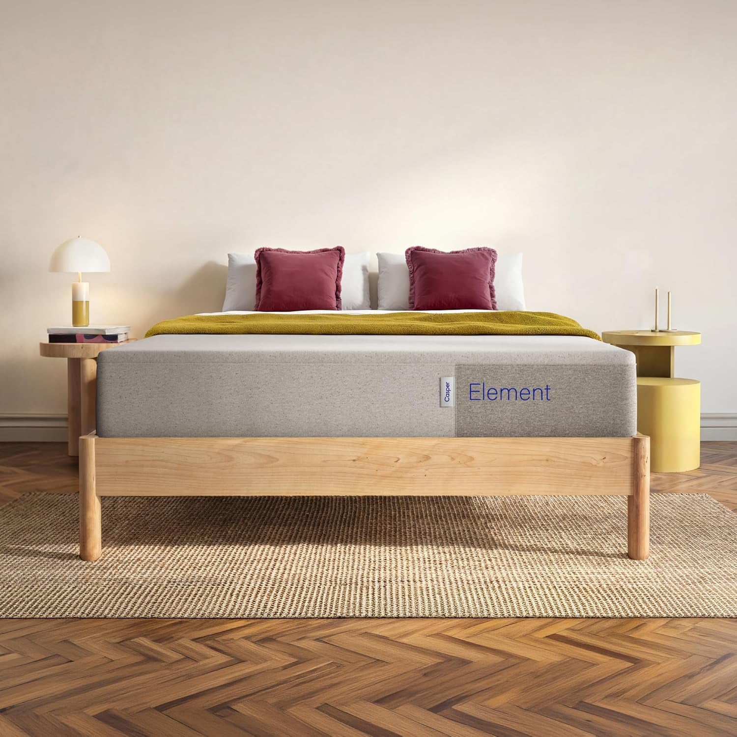 Front bedroom view of a light-gray mattress on a low wooden frame with burgundy pillows and a mustard throw.