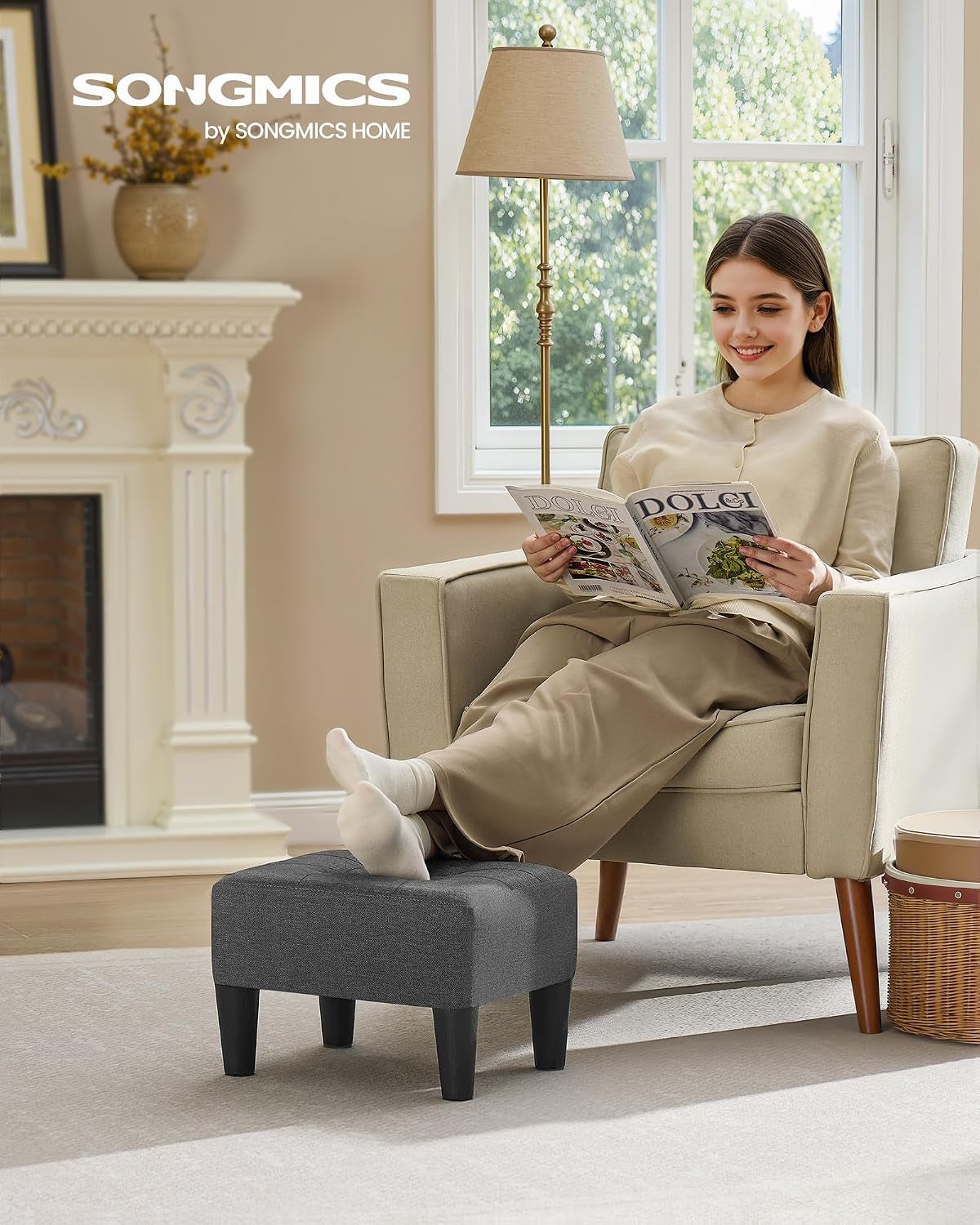 Dark gray ottoman used as a footrest in a living room setting with a woman reading in an armchair