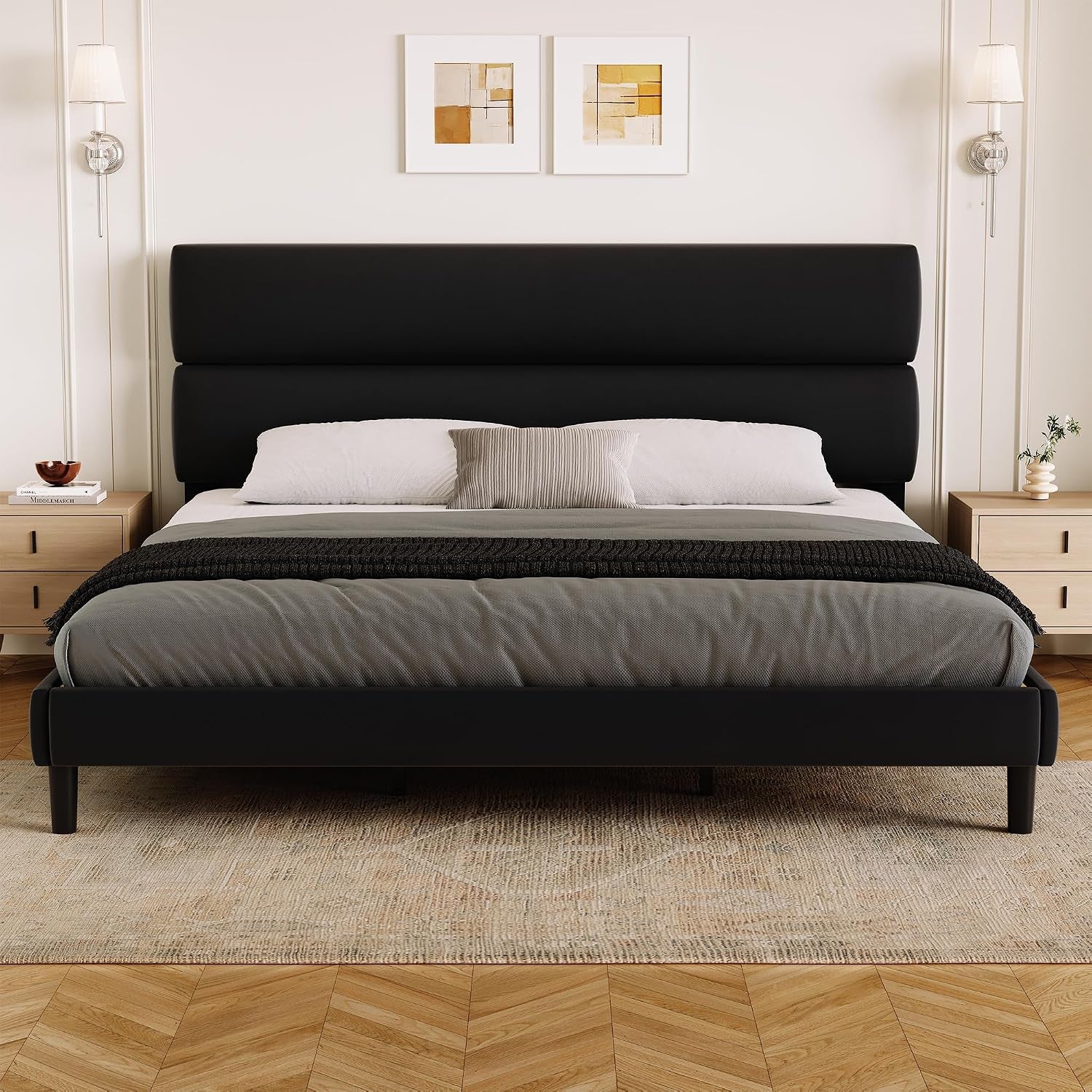 Wide front room shot of a black upholstered bed with a tall two-panel headboard.