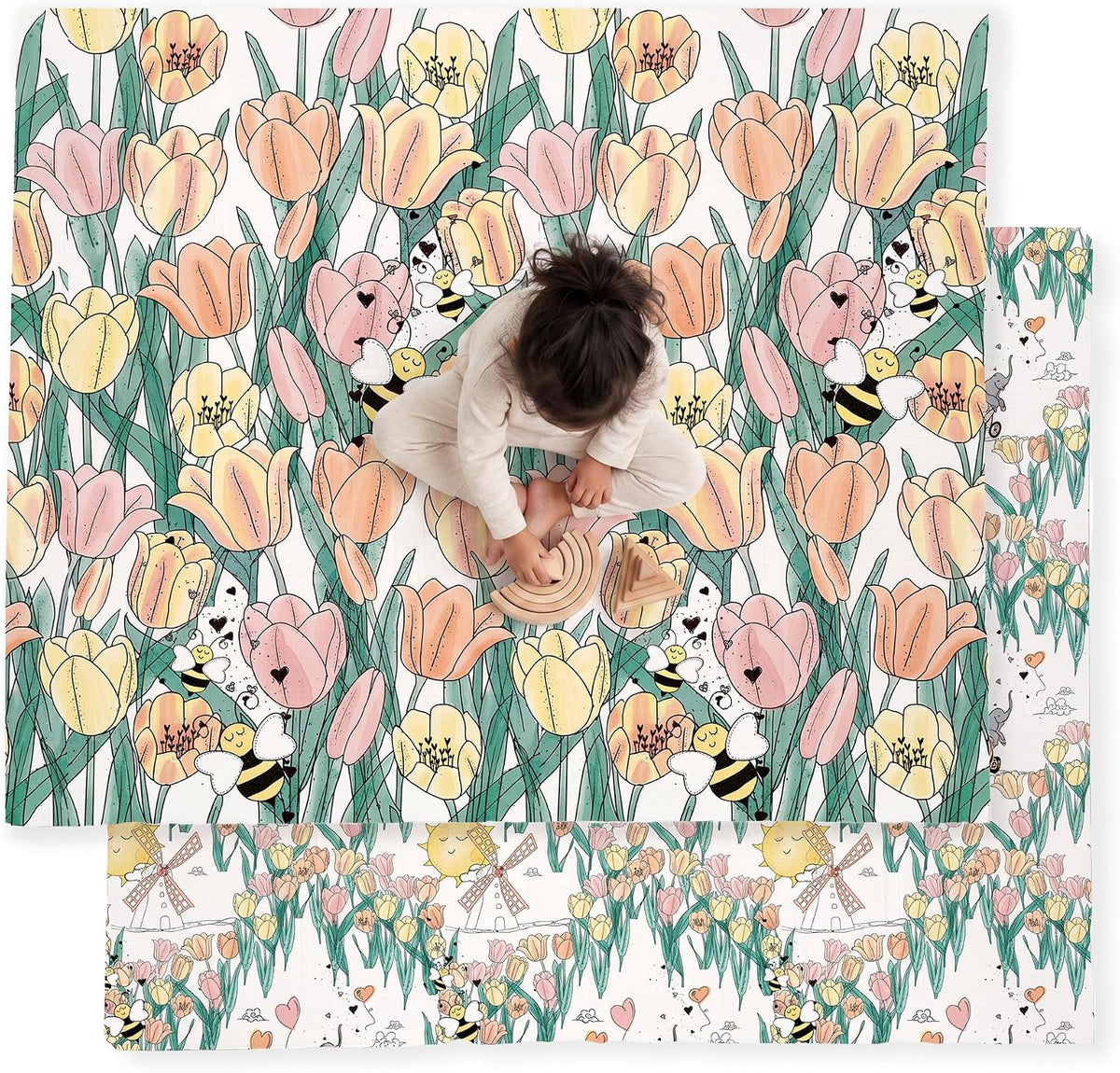 Top-down shot of a toddler on a dense tulip-and-bee patterned mat in soft pinks and greens with a windmill-themed reverse