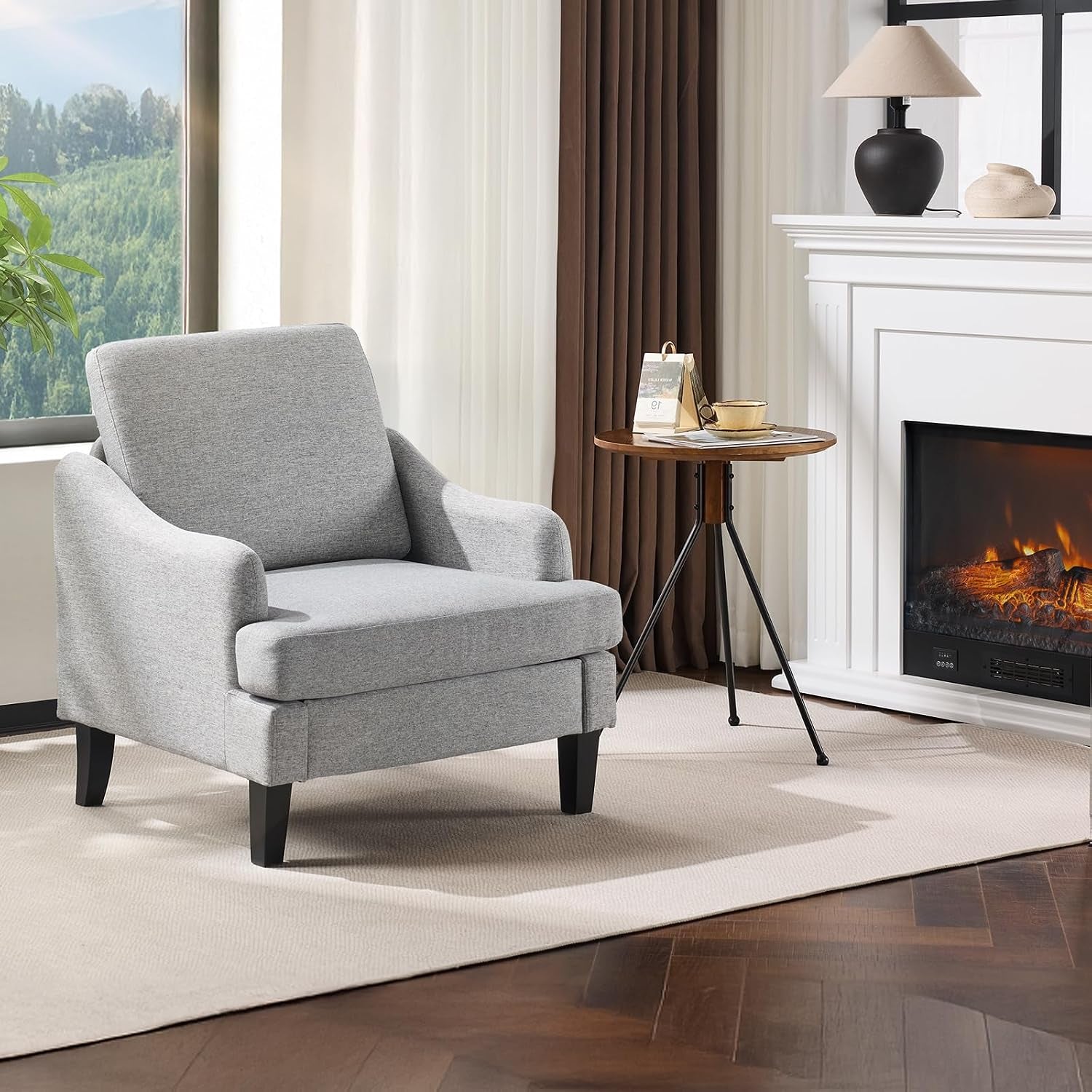 Single light gray upholstered armchair beside a round side table and fireplace.