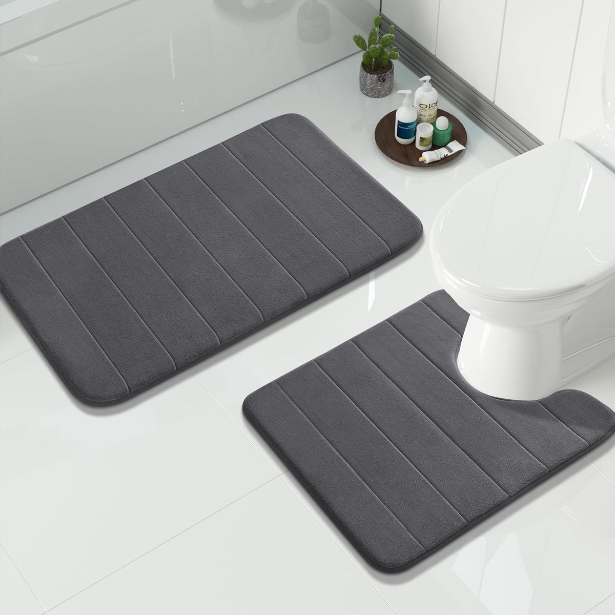 Two charcoal-gray bath mats, one contoured around a white toilet and one larger mat beside a bathtub.