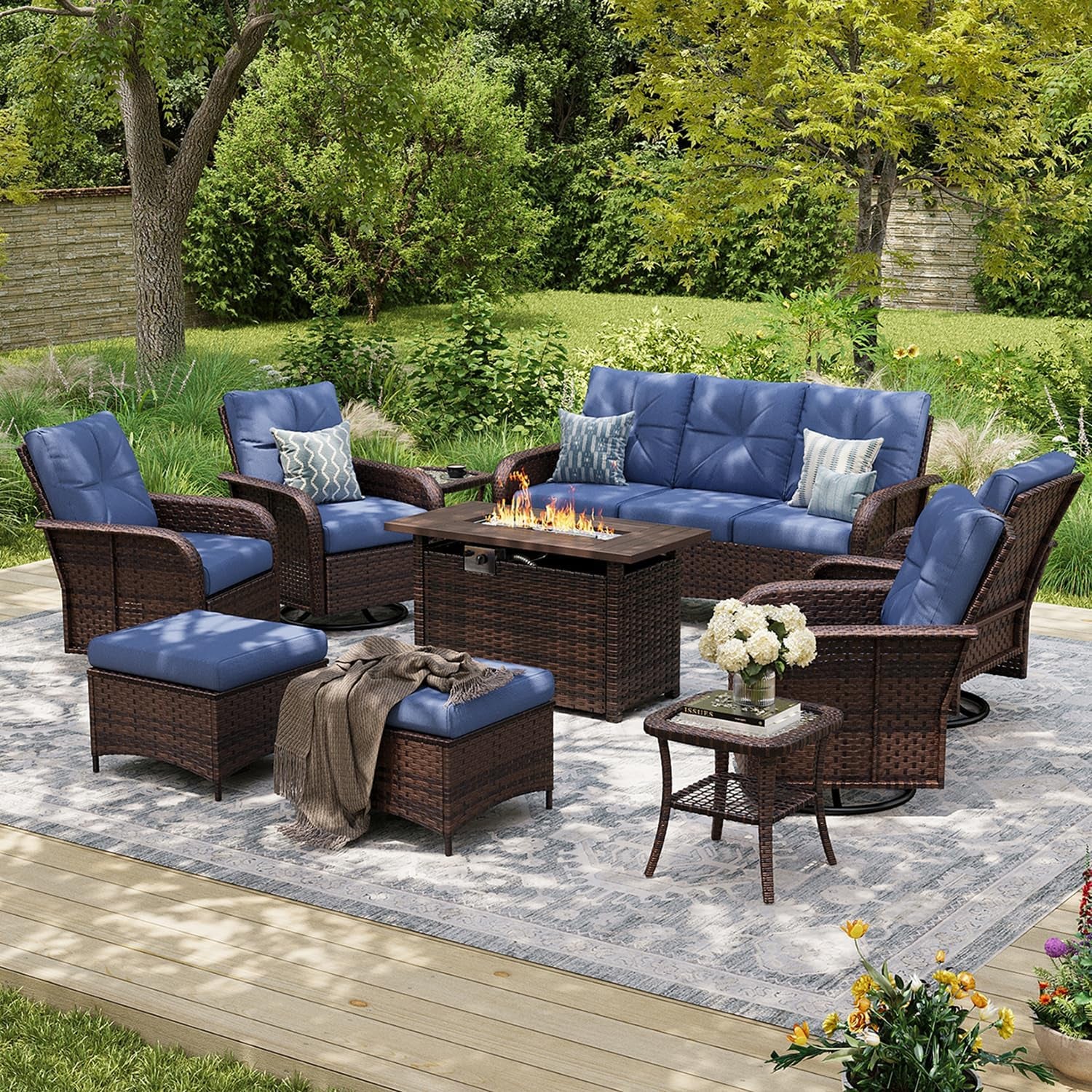 Outdoor patio set on a rug with blue-cushioned sofa, swivel chairs, ottomans and a rectangular fire pit table