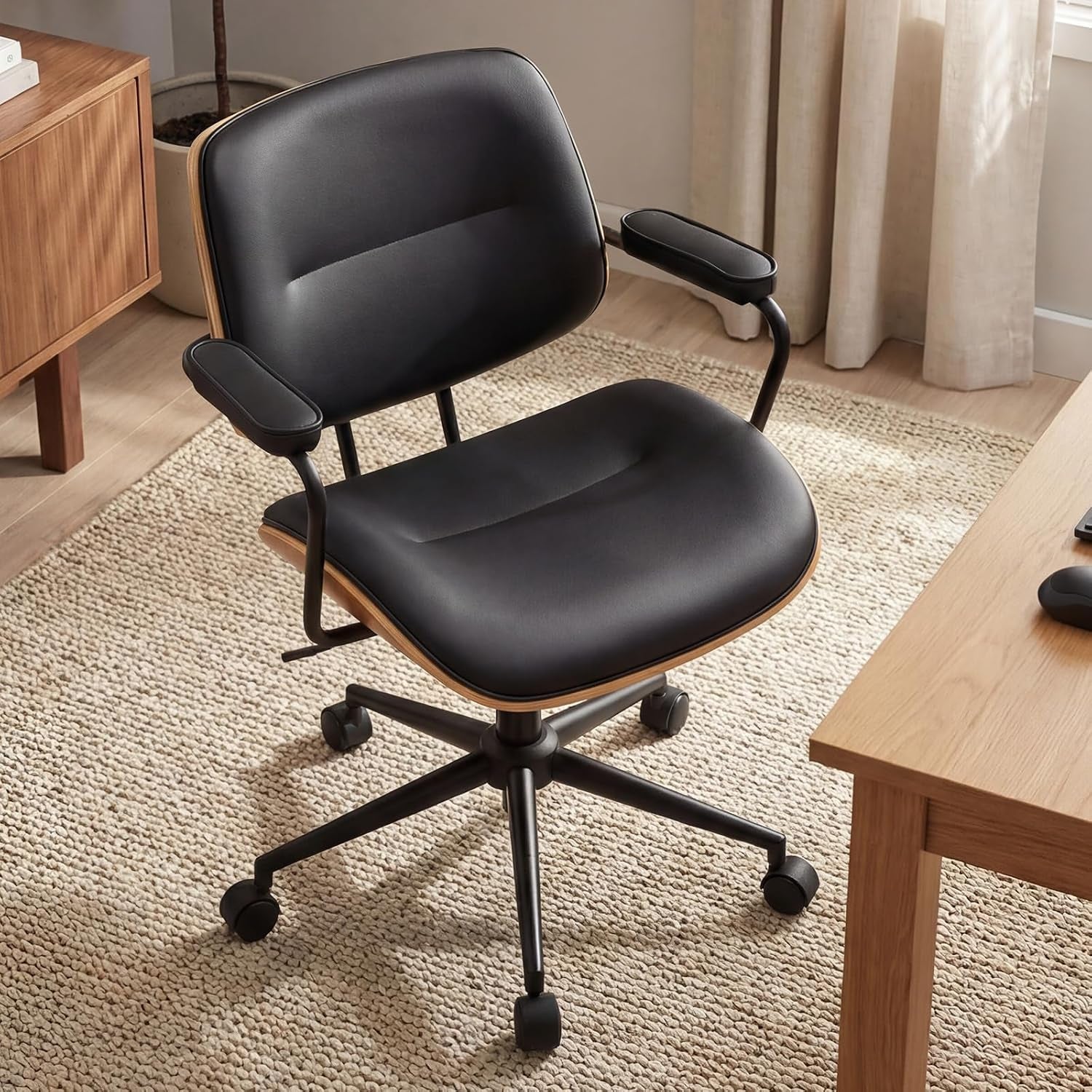 Black version of the same mid-century office chair placed on a textured rug next to a desk