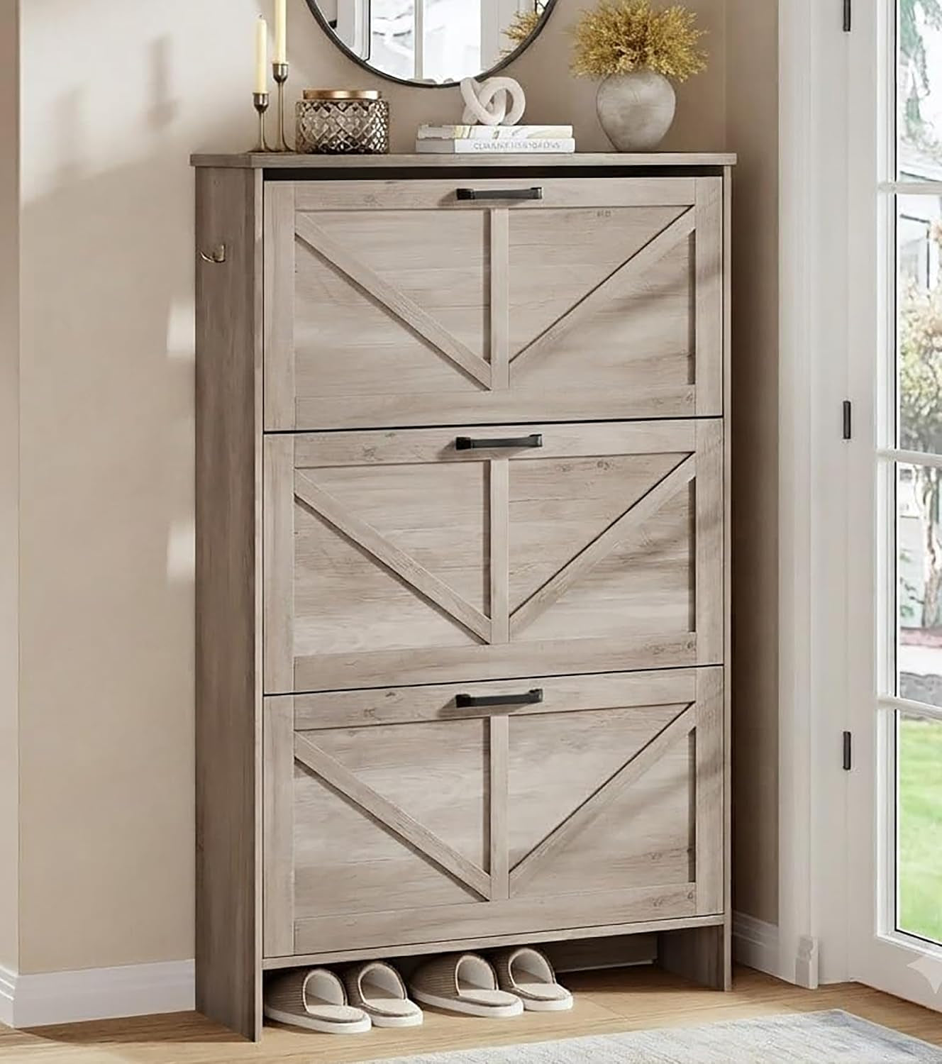 Three-quarter view of a weathered gray three-drawer shoe cabinet with X-mullion drawer fronts and decor on the top surface.