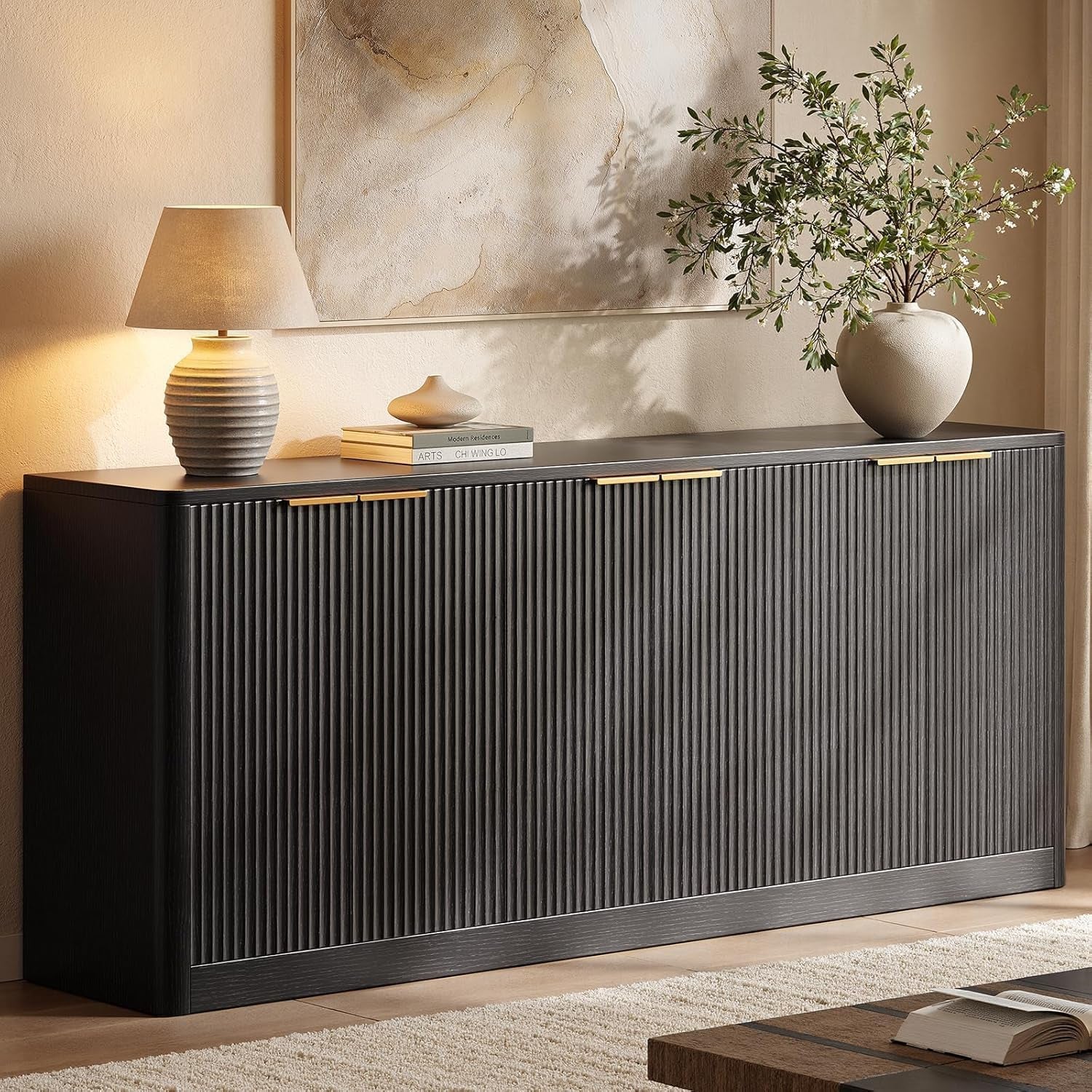 Black fluted sideboard styled with lamp, books, and a vase in a softly lit room