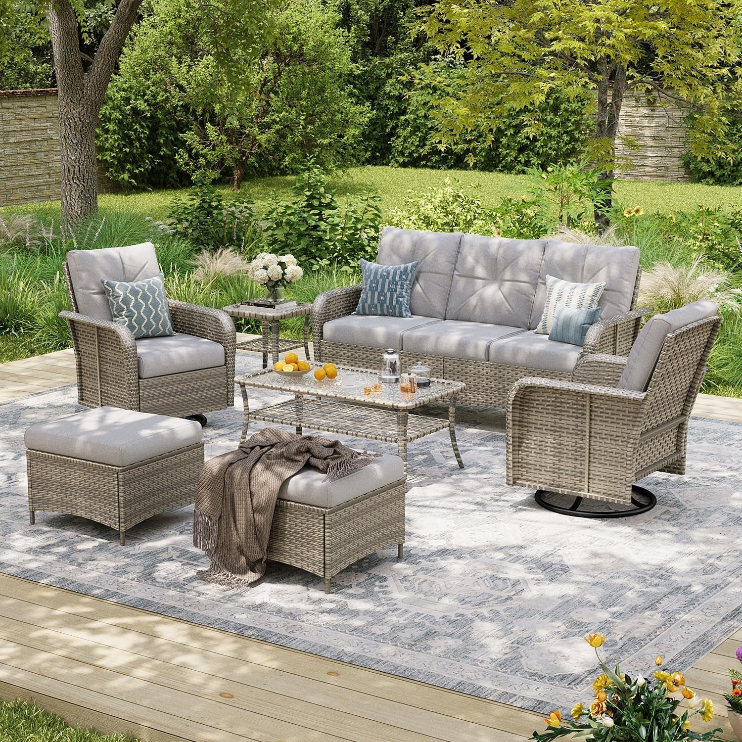 Beige wicker patio set with three-seat sofa, two swivel chairs, coffee table and two ottomans on an outdoor rug.