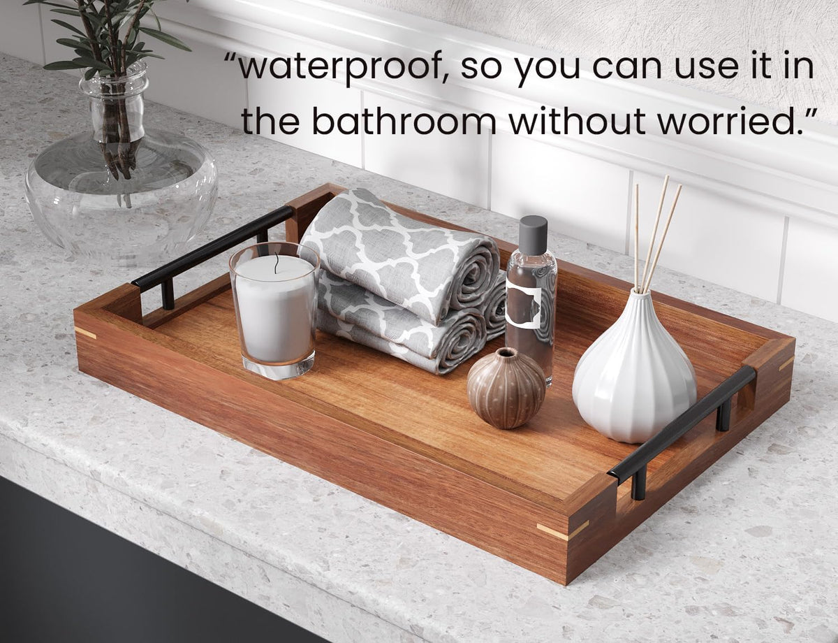 Brown acacia tray with black handles on a bathroom counter holding rolled towels, candle, and bottle