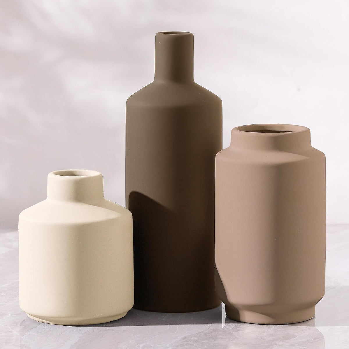 Tight close-up of three matte ceramic vases showing necks, silhouettes and soft shadows.