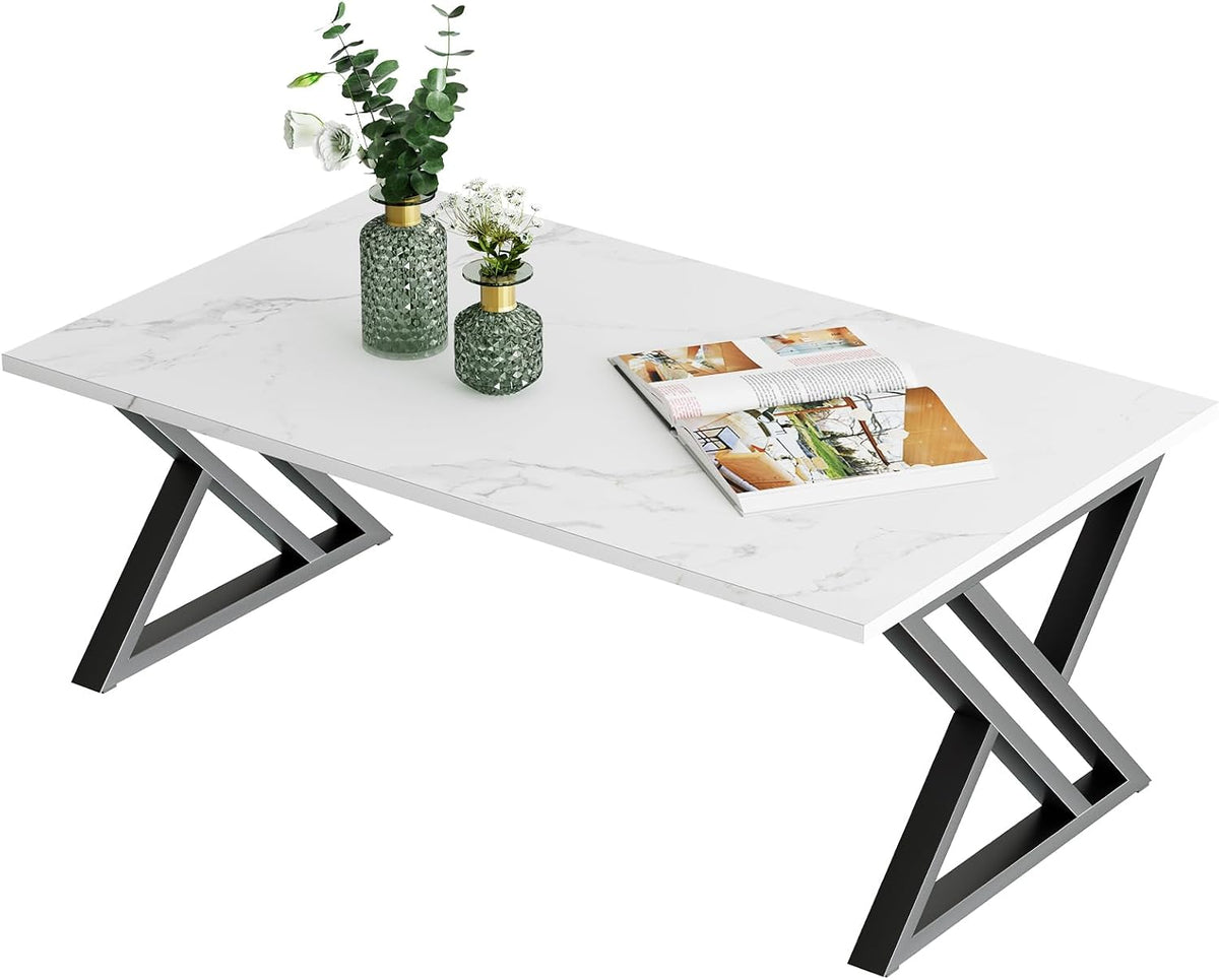 Angled studio shot of a rectangular white faux-marble tabletop with dark X-shaped steel legs, magazine and vases on top