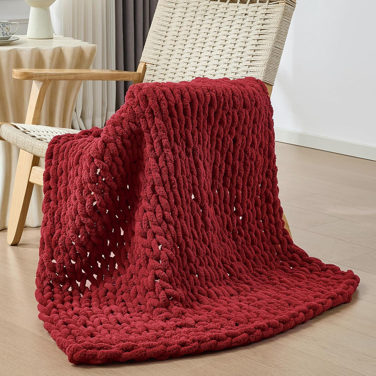Deep red chunky knit throw draped over a woven-seat chair, cascading onto the floor.