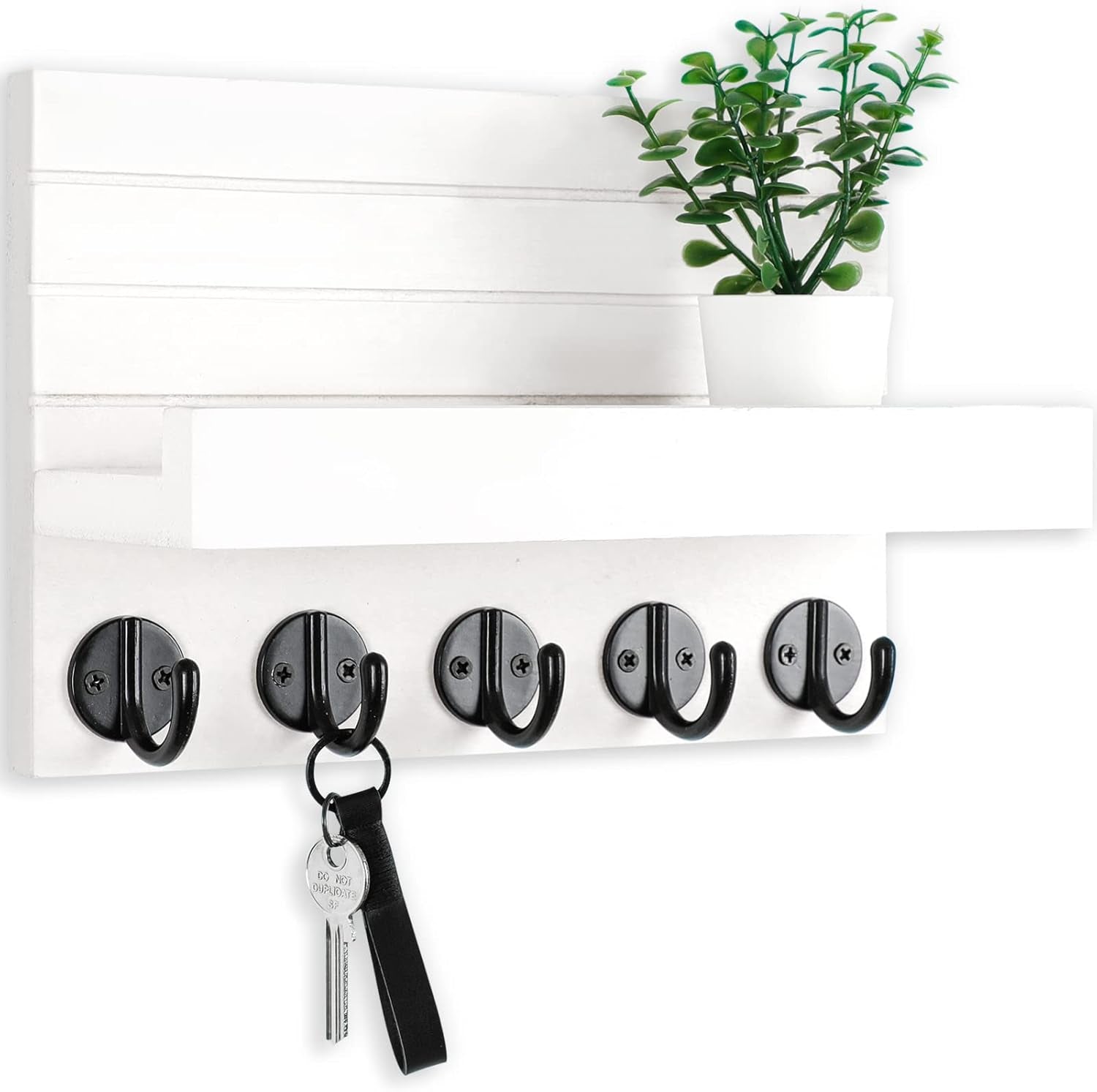 White wall key holder with five black hooks, a shelf, potted plant, and hanging key.