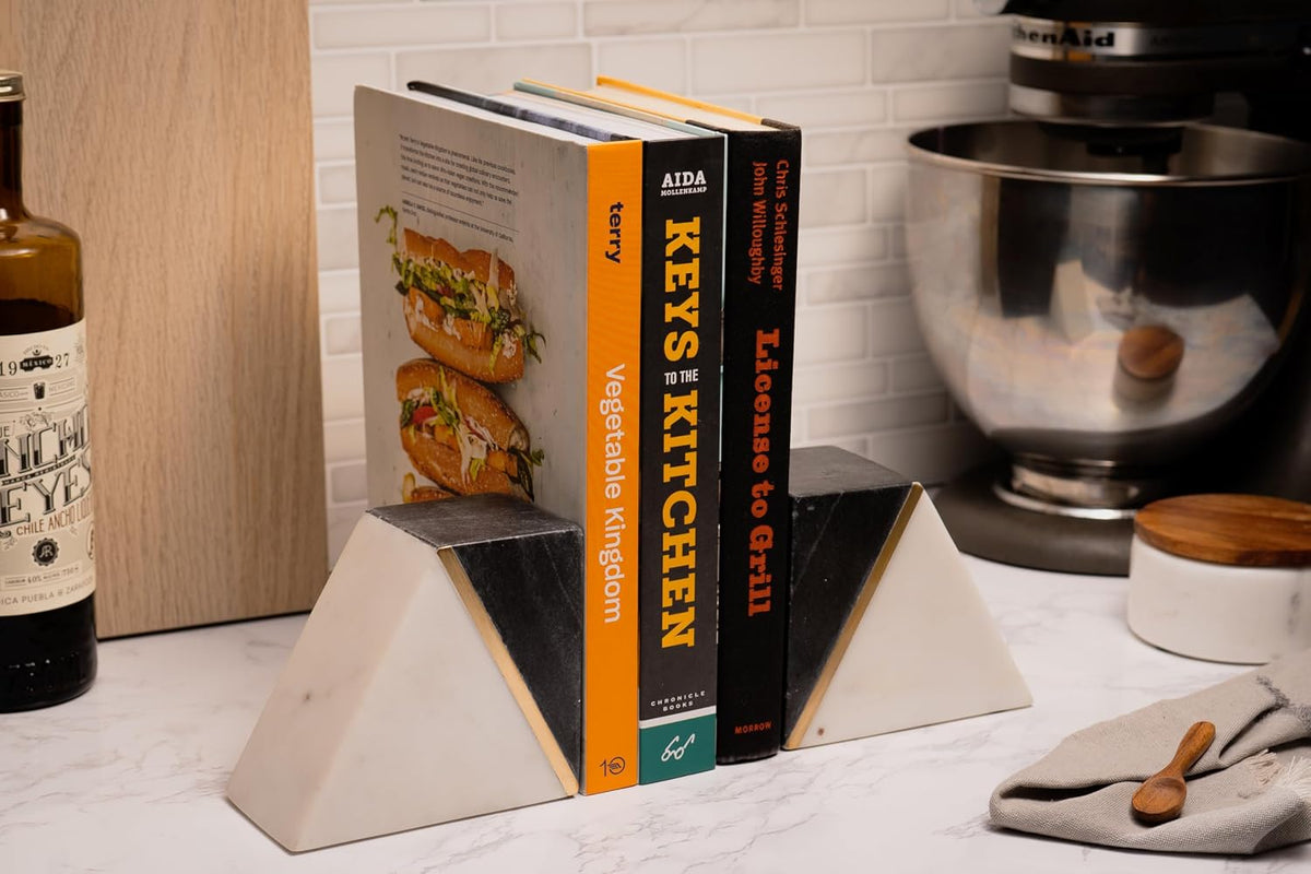 Bookends on a kitchen counter holding cookbooks, pictured next to a mixer and small jar