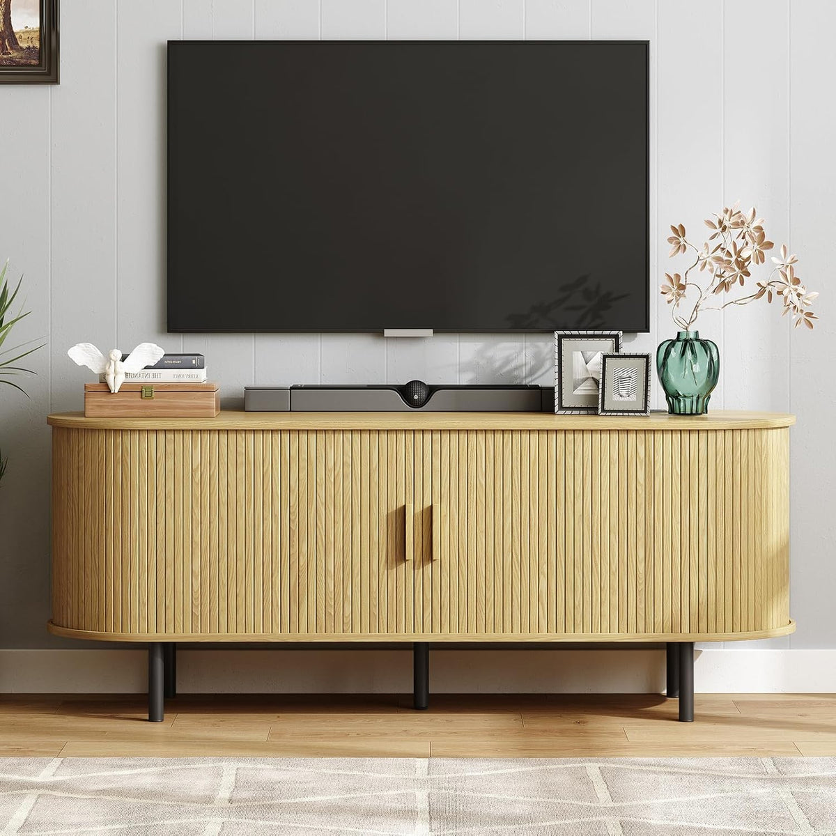 Light blond ribbed TV stand with rounded ends and black legs, styled with books and a green vase.
