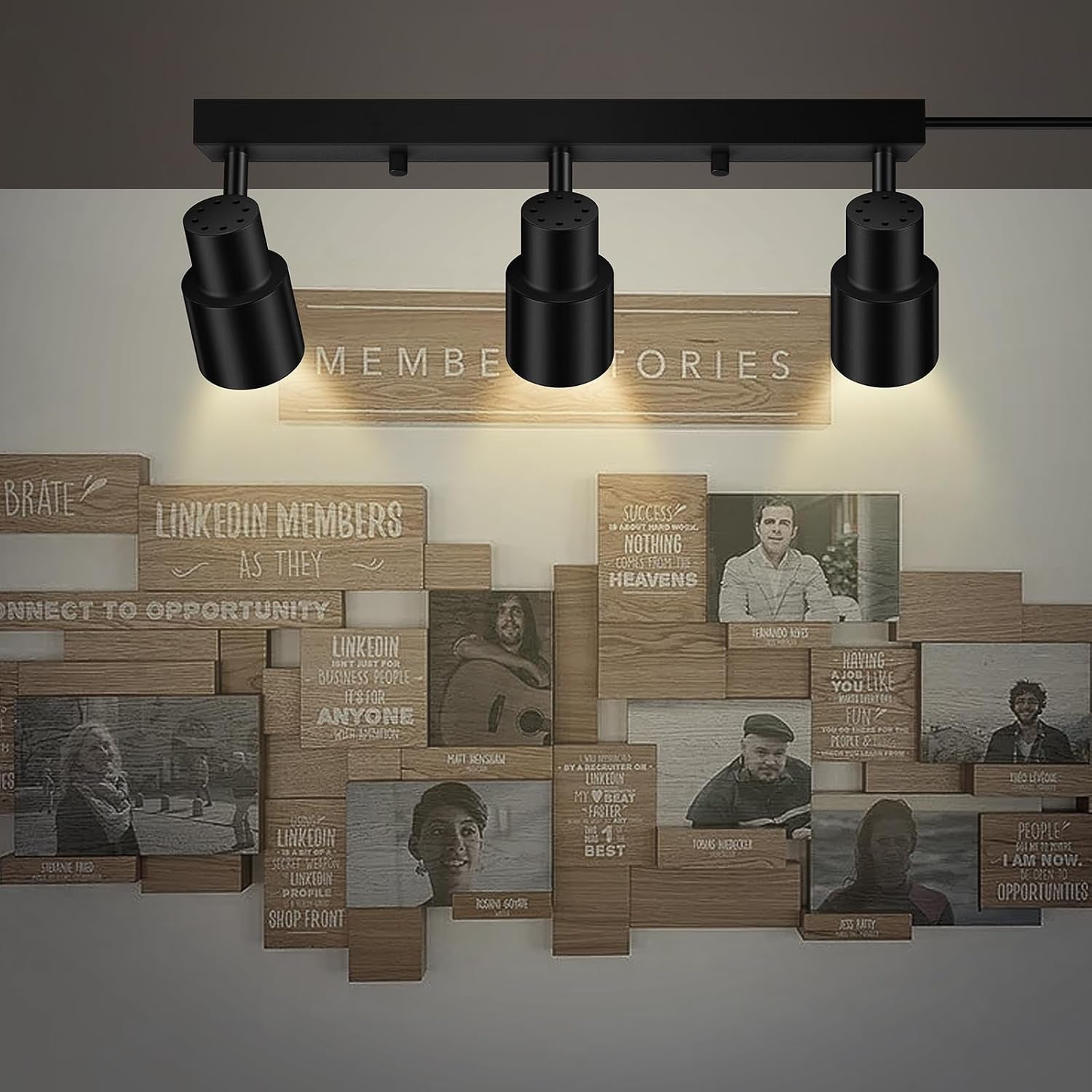 Black three-light ceiling track with three cylindrical adjustable spotlights lighting a wooden photo collage on the wall.