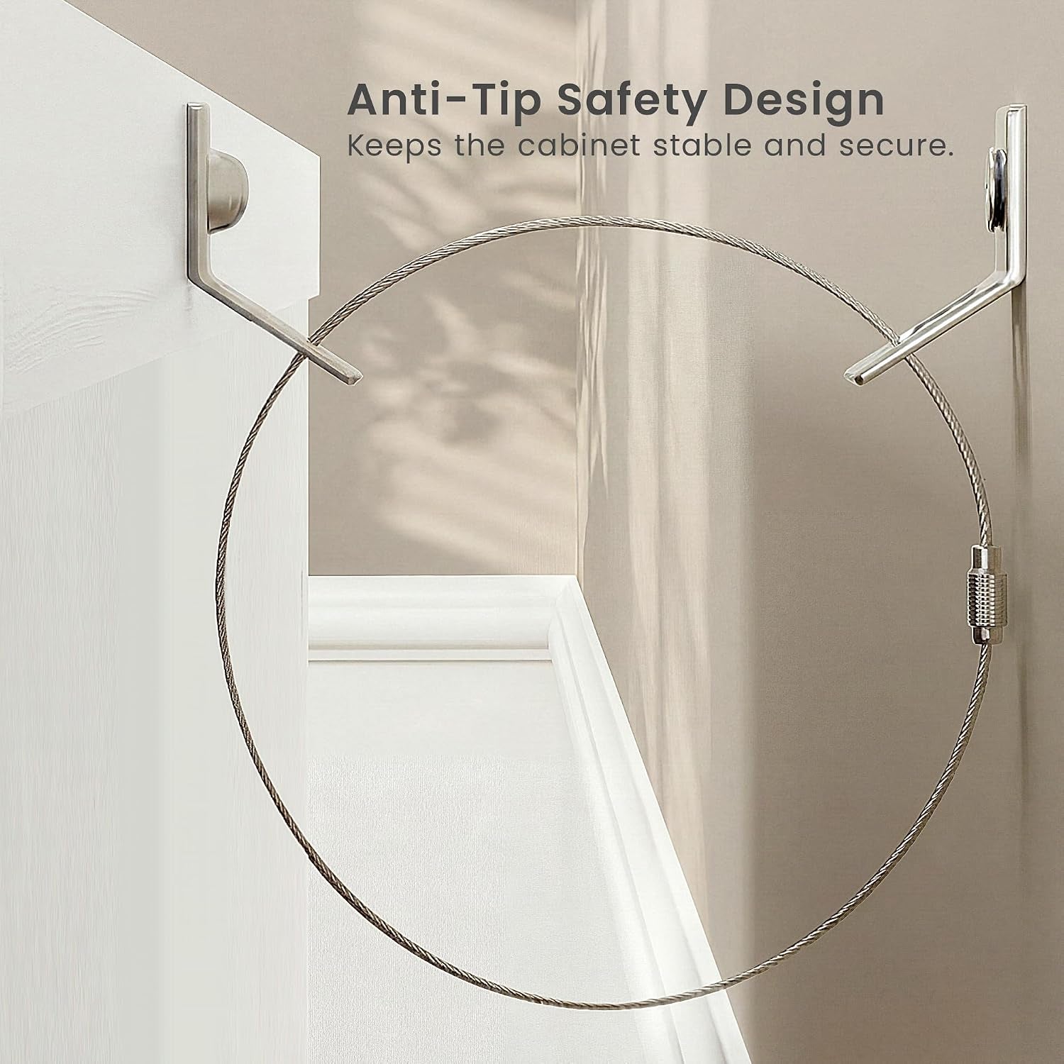 Close-up of a metal anti-tip cable looped between two wall anchors at the back corner of a white cabinet.