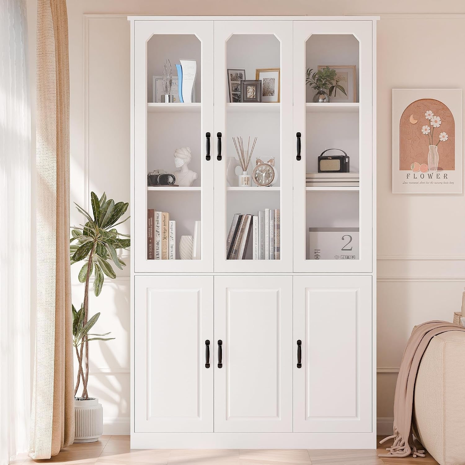 Full-height white pantry with three glass doors, styled with books and decor, plant at left and framed art at right.