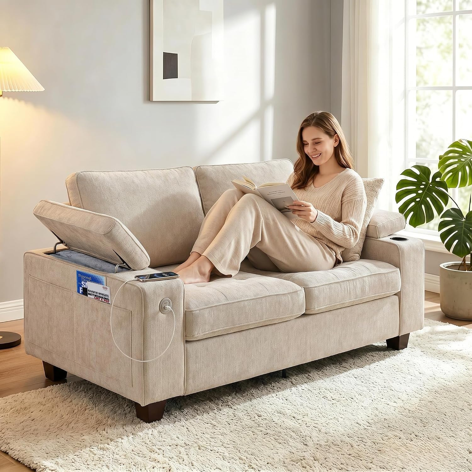 Woman reading on a beige loveseat with the left armrest flipped up to reveal storage and a visible USB cable.