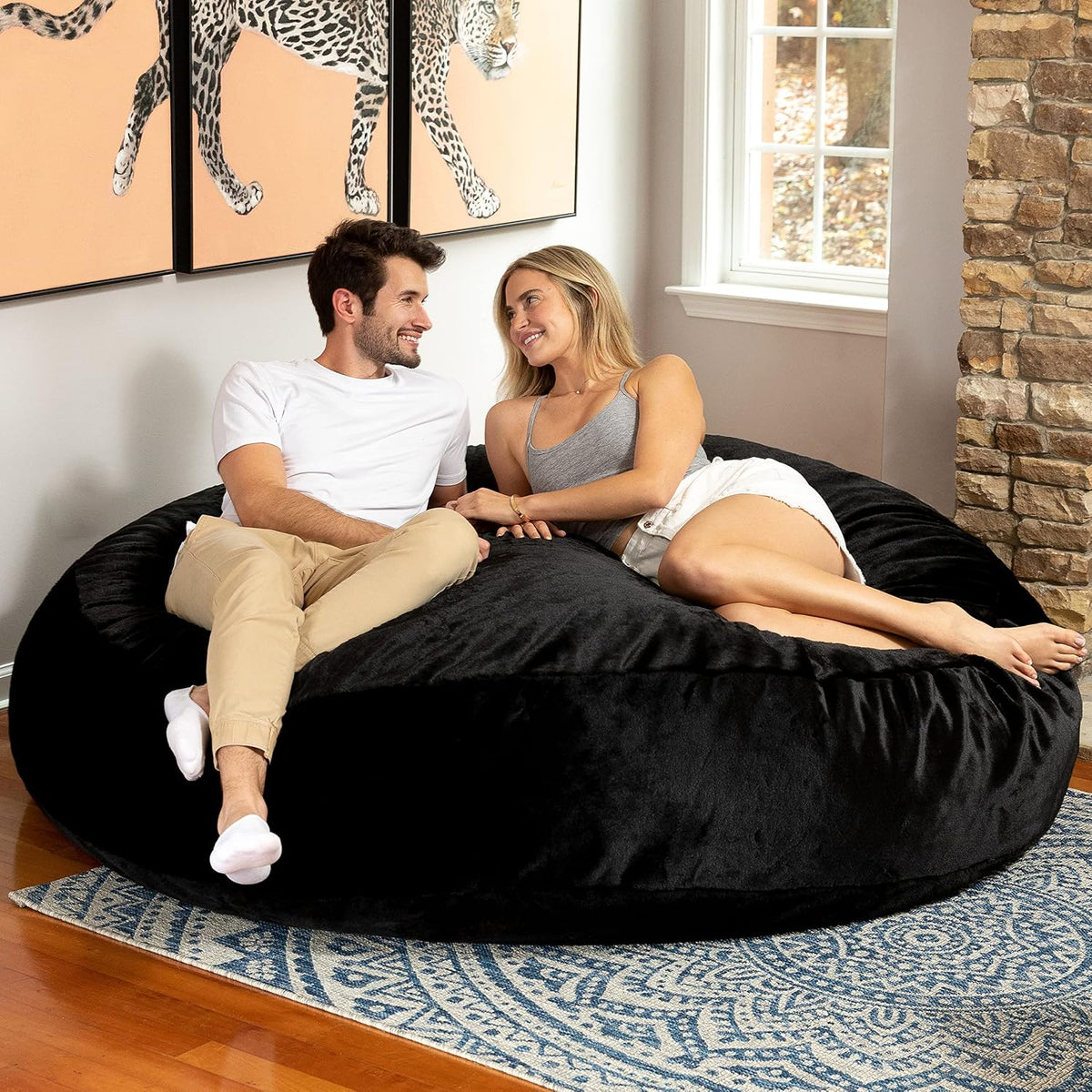 Black round bean bag on a patterned rug with a couple leaning and smiling together