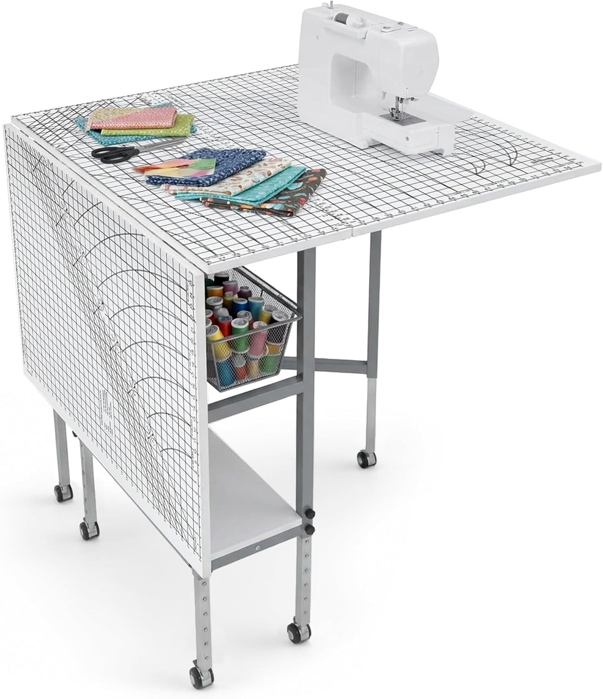 Angled view of a folding craft table with grid top, sewing machine, stacked fabric and a mesh drawer visible