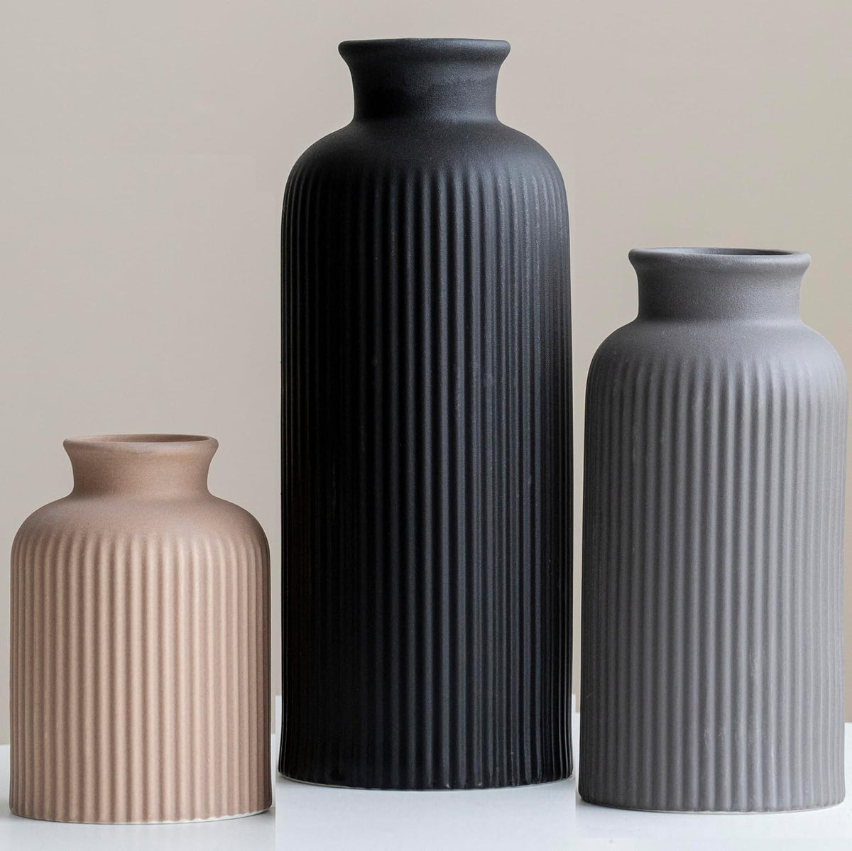 Three ribbed matte vases in muted taupe, black, and gray lined up against a neutral backdrop.