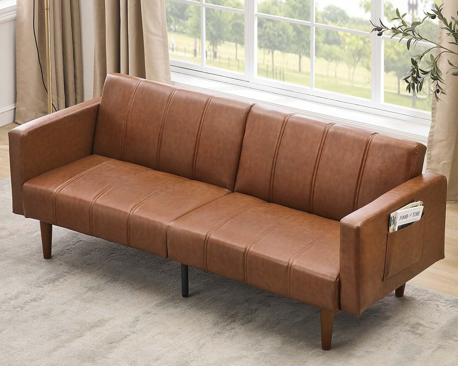 Three-seat brown PU leather futon sofa in a sunlit room, shown upright with tapered wooden legs.