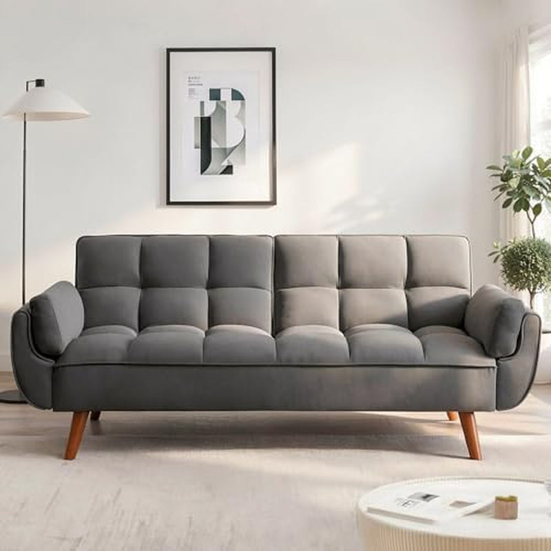 Gray tufted futon sofa with rounded arm cushions and tapered wooden legs under a framed abstract print.