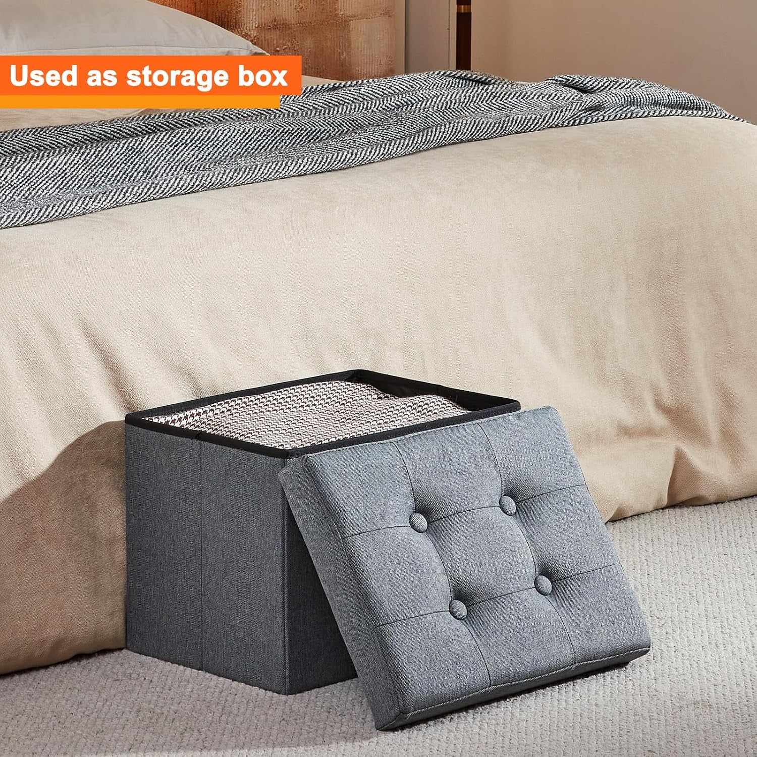 Grey ottoman with removable tufted lid beside a bed showing open interior storage