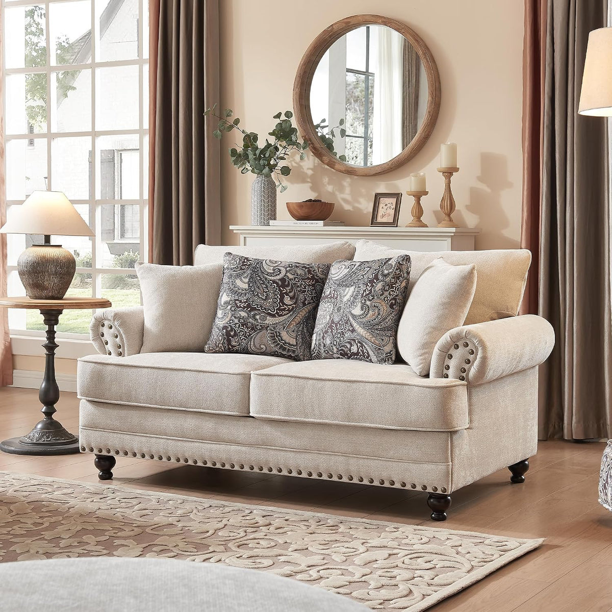 Beige chenille loveseat with rolled arms, nailhead trim and paisley accent pillows beside a lamp.