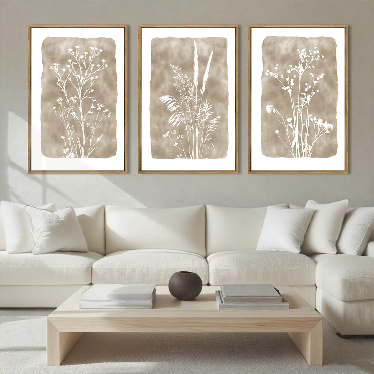 Three framed prints showing beige watercolor panels with white botanical silhouettes above a cream sofa.