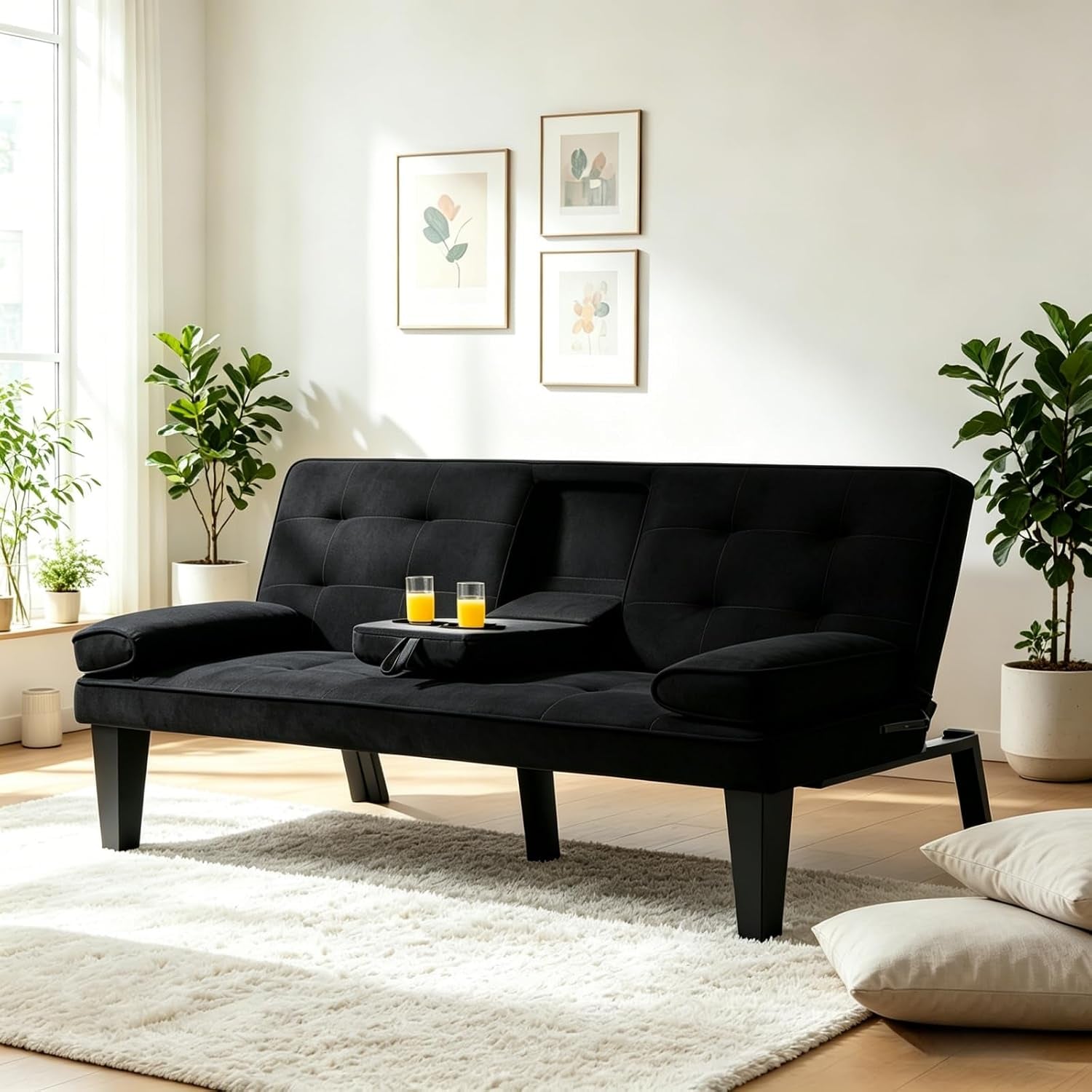 Black velvet futon sofa in bright room with tufted back, center armrest tray holding two glasses of orange juice.
