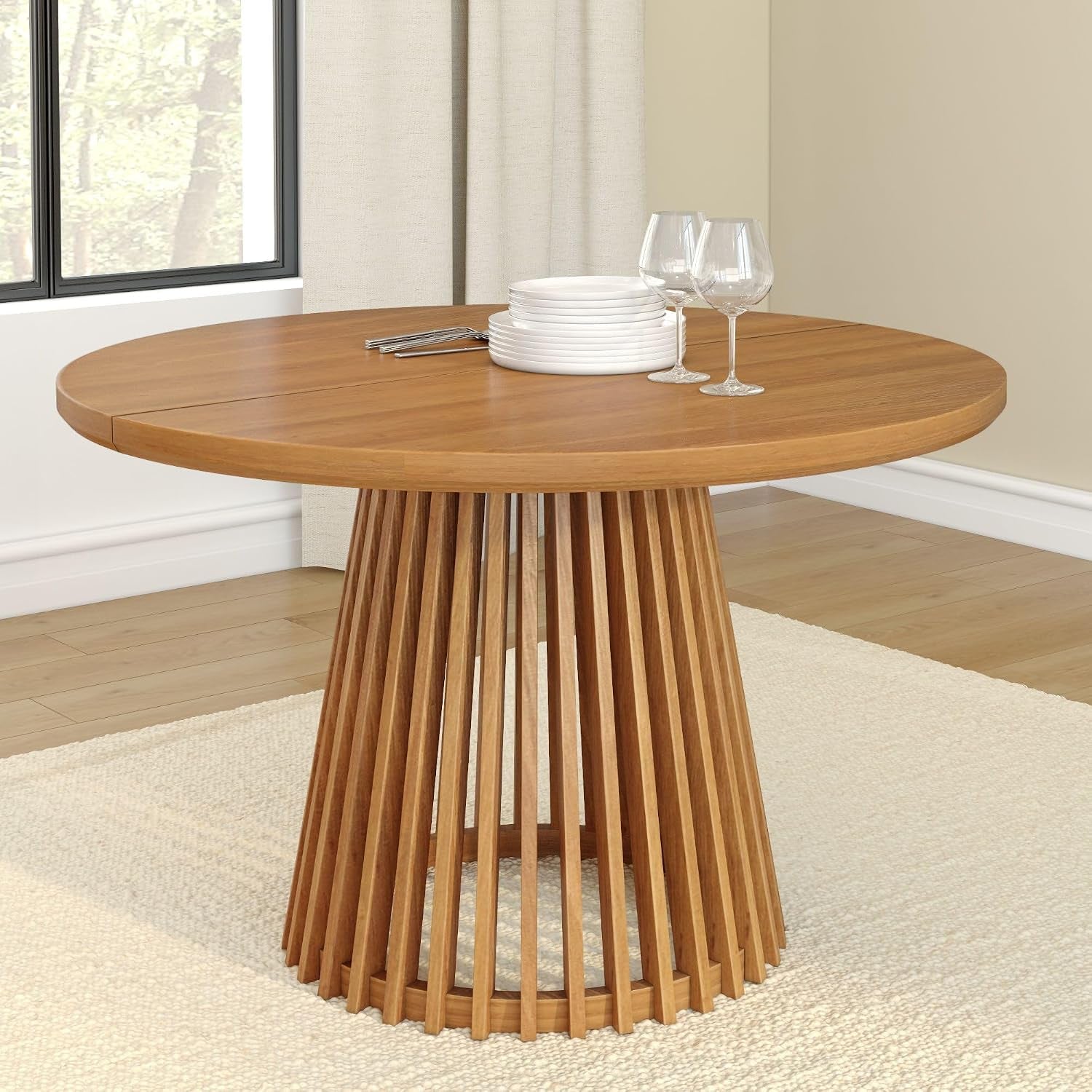 Round honey-toned wood dining table with slatted pedestal base and stacked plates on top.