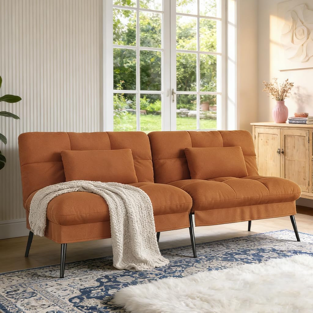 Warm terracotta-colored futon sofa with matching pillows and a light knit throw on a patterned rug.
