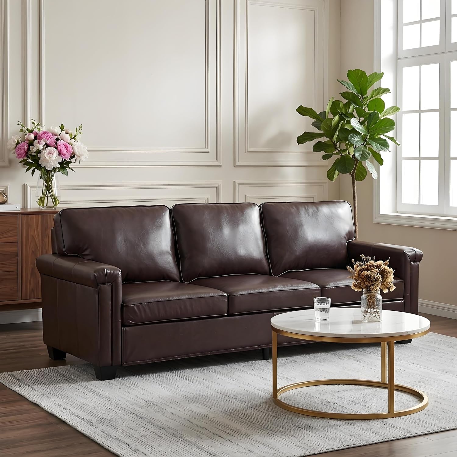 Three-seat dark brown leather sofa in a living room with round coffee table and plant.