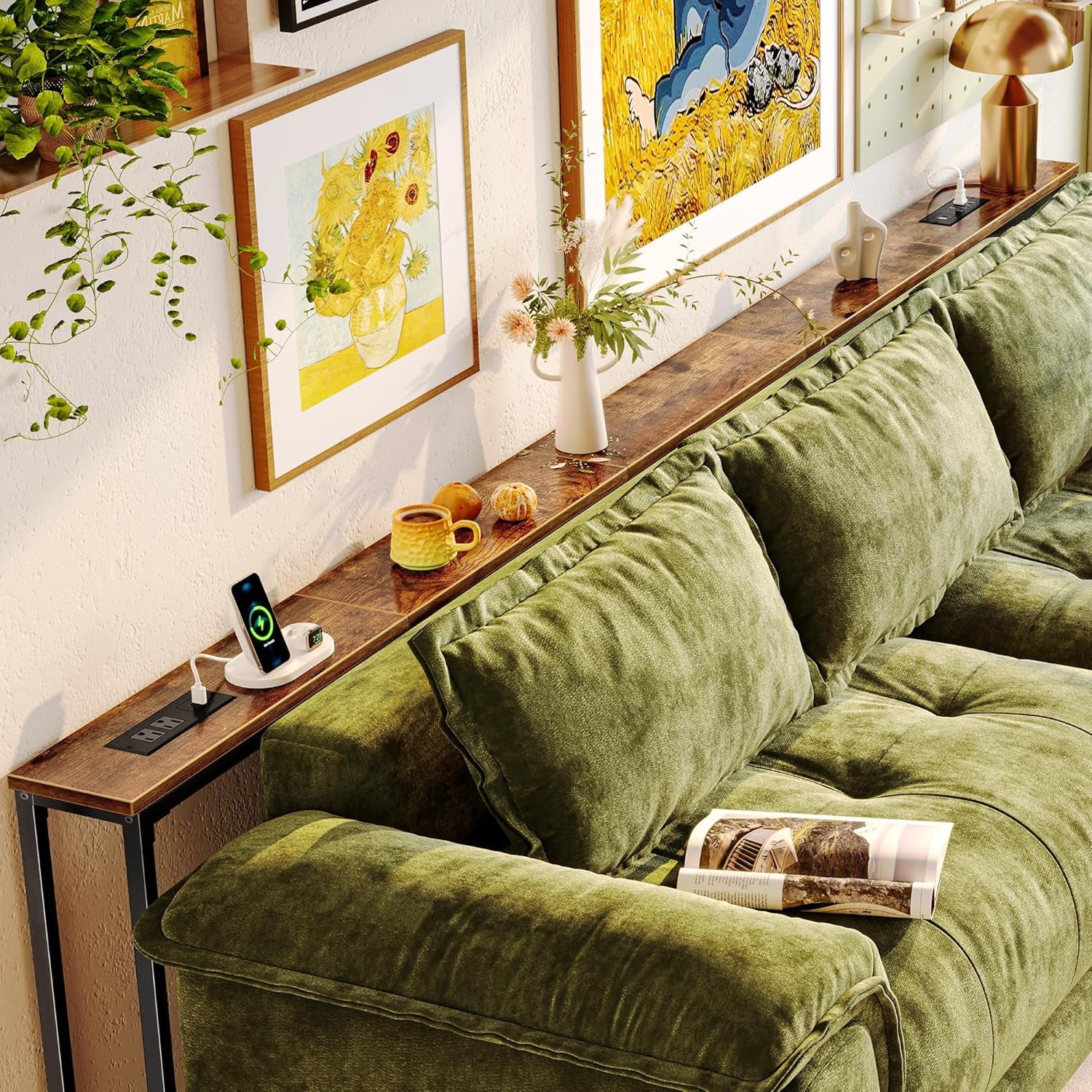 Extra-long rustic brown sofa table behind a green couch holding a lamp, vase and charging dock.