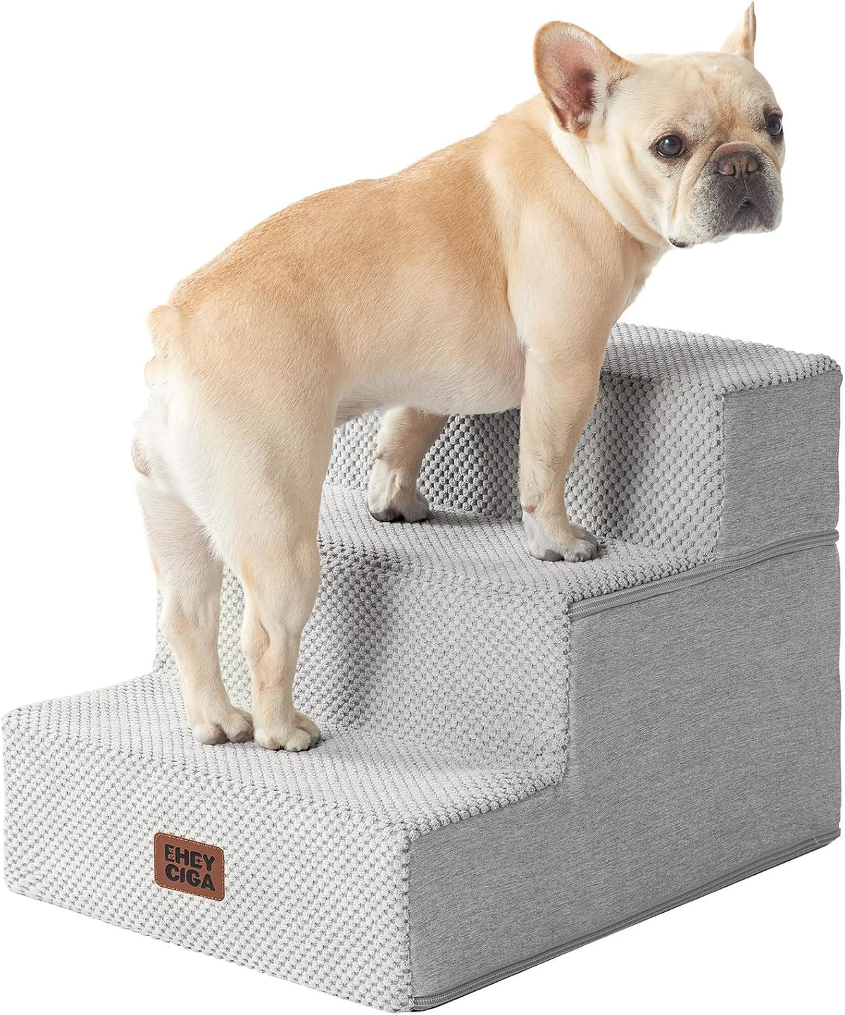 Light-colored French bulldog standing on light-gray four-step foam stairs, textured cover and zipper visible