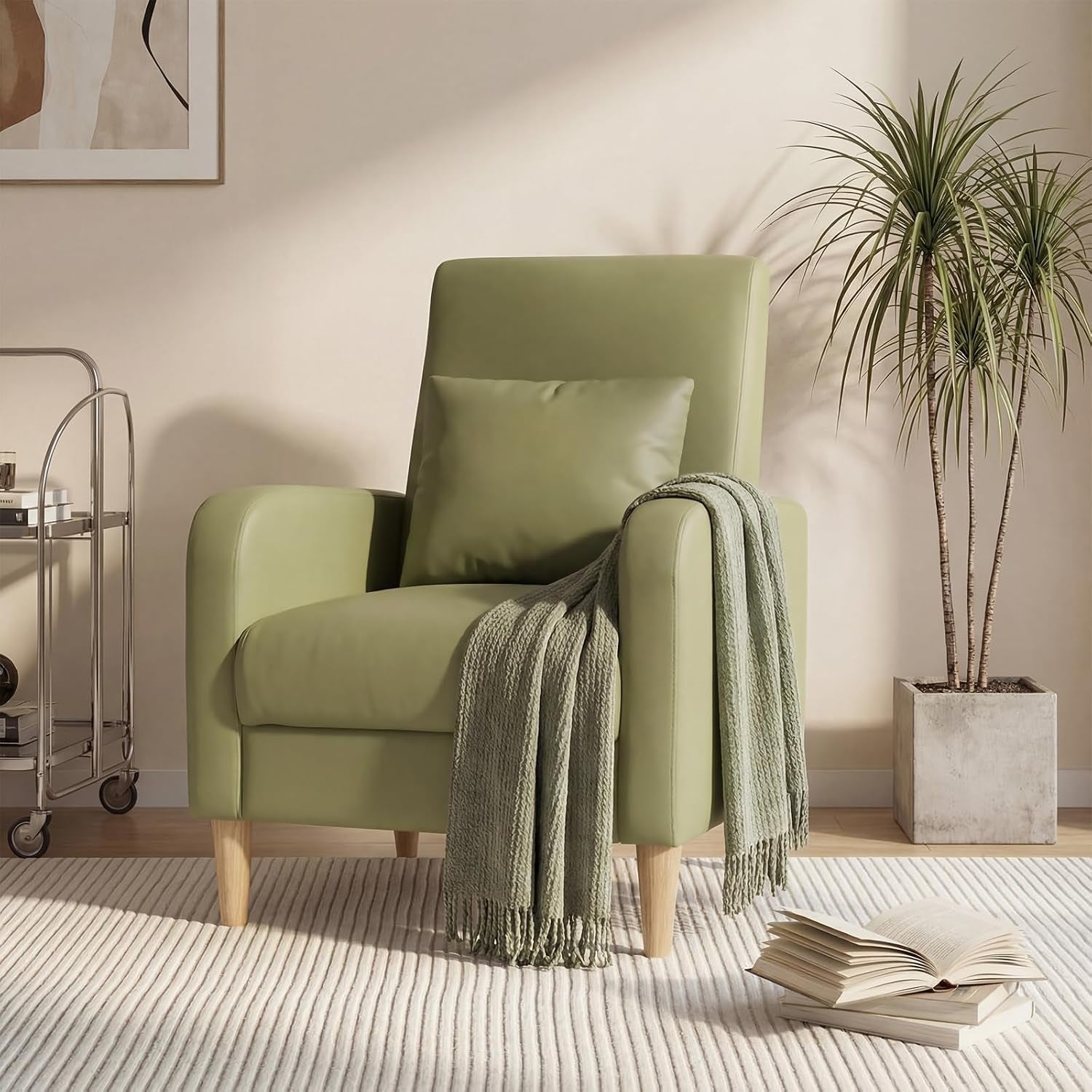 Single pale green fabric armchair with wooden legs, pillow and knit throw beside a potted plant