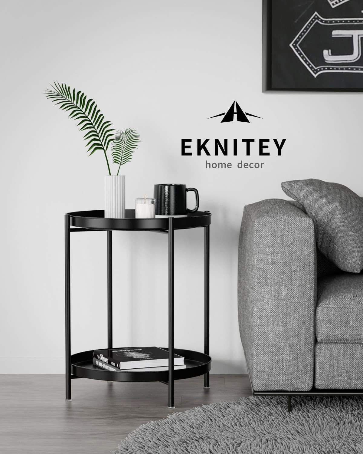 Black two-tier round metal side table beside a gray sofa with a vase, mug, and books on its tiers.