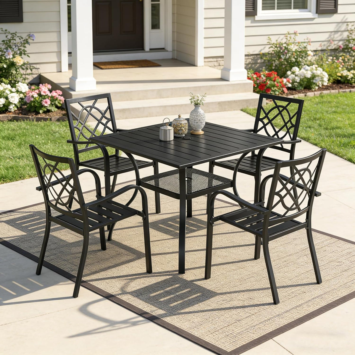 Black square table and four matching chairs arranged on a patio rug with house steps in the background