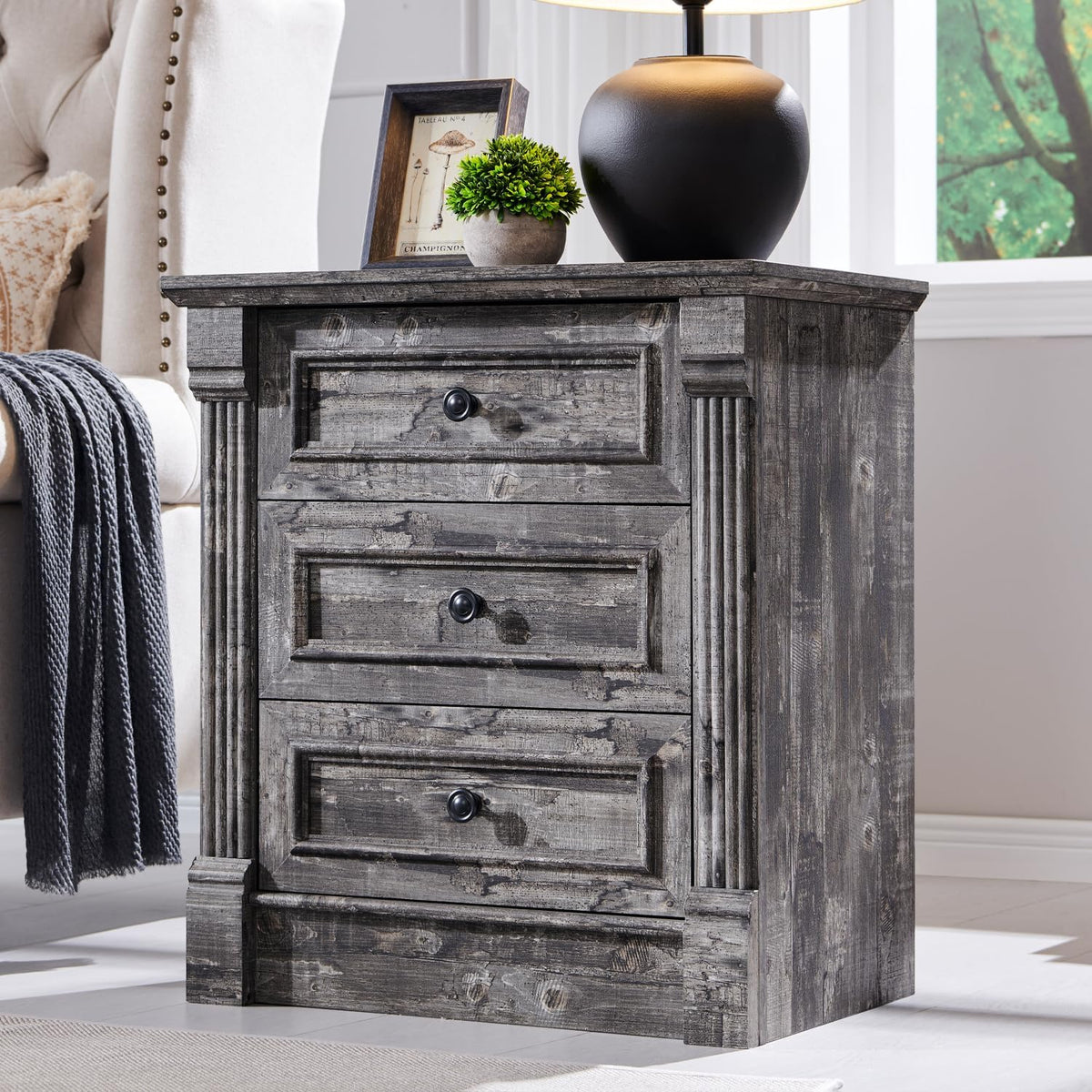 Close angled view of a gray wood three-drawer nightstand with fluted column details on the sides.