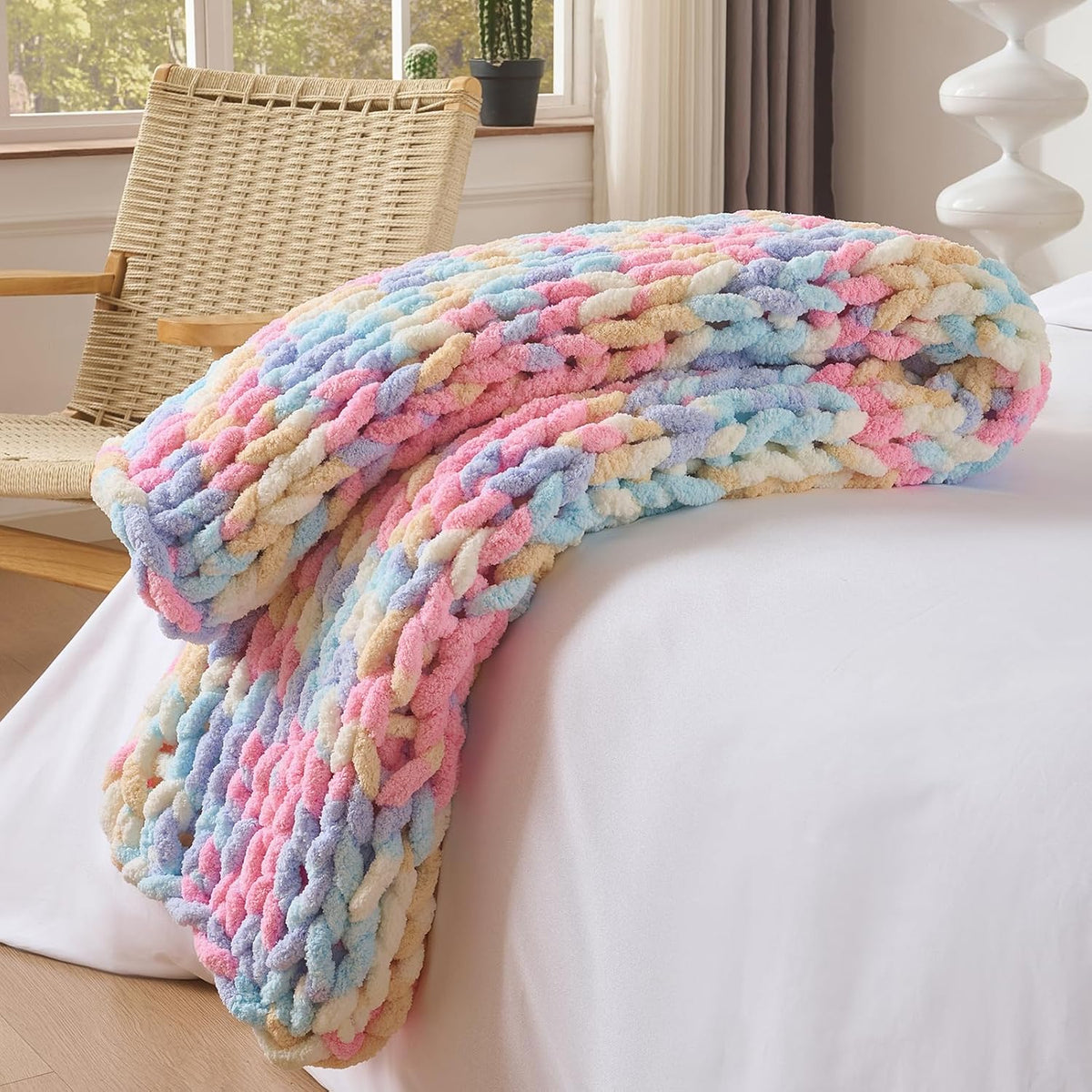 Pastel multicolor chunky knit throw folded and draped over a white mattress edge.