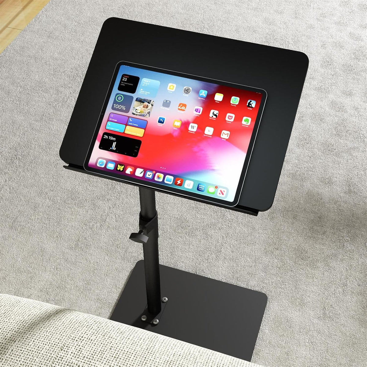 Black tabletop from above with a tablet resting on its surface, showing the table's swivel post and base.