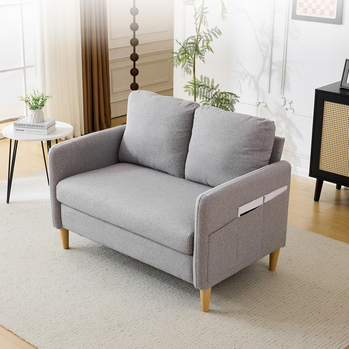 Light grey linen loveseat front-left view in a styled living room with side table, plant, and rug