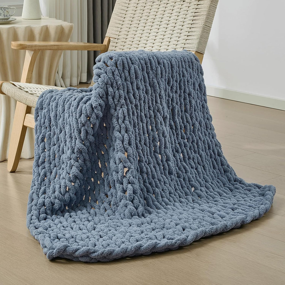 Slate-blue chunky knit throw cascading from a woven chair onto the floor.