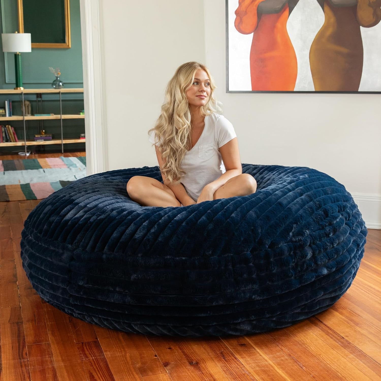 Woman sitting cross‑legged on a ribbed navy blue round bean bag in a bright room.