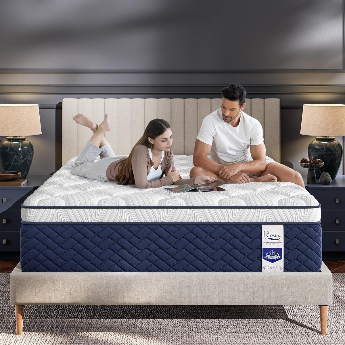 Front view of a navy-sided hybrid mattress on a beige platform bed with two people lounging on top.