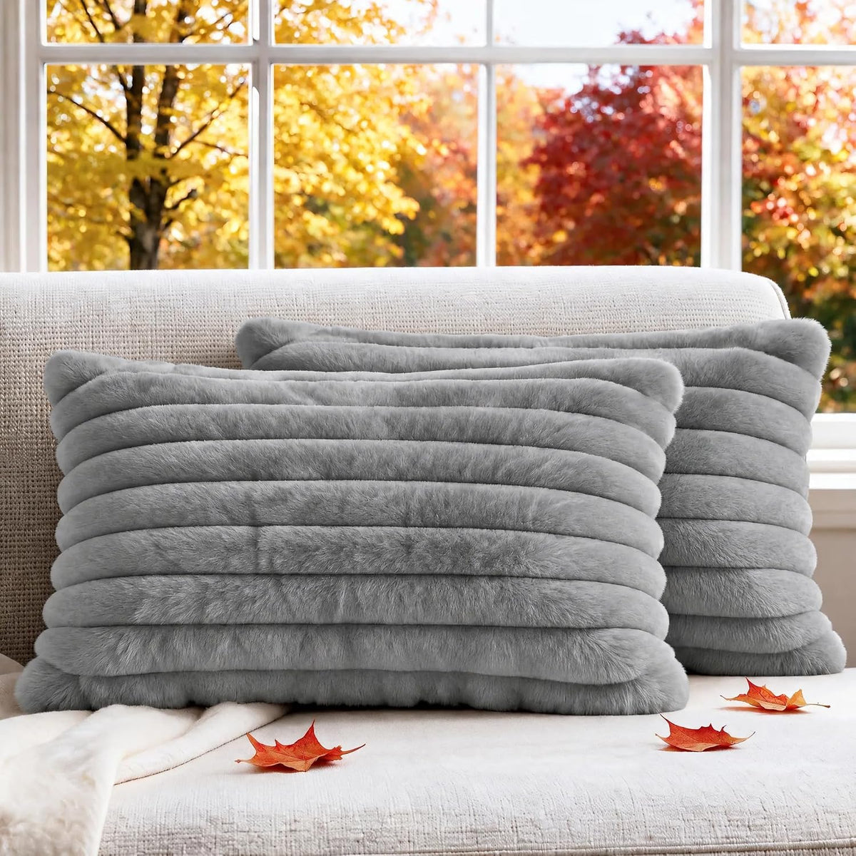Close view of two horizontal-ribbed faux-fur pillows in medium gray leaning on a sofa with fall leaves.