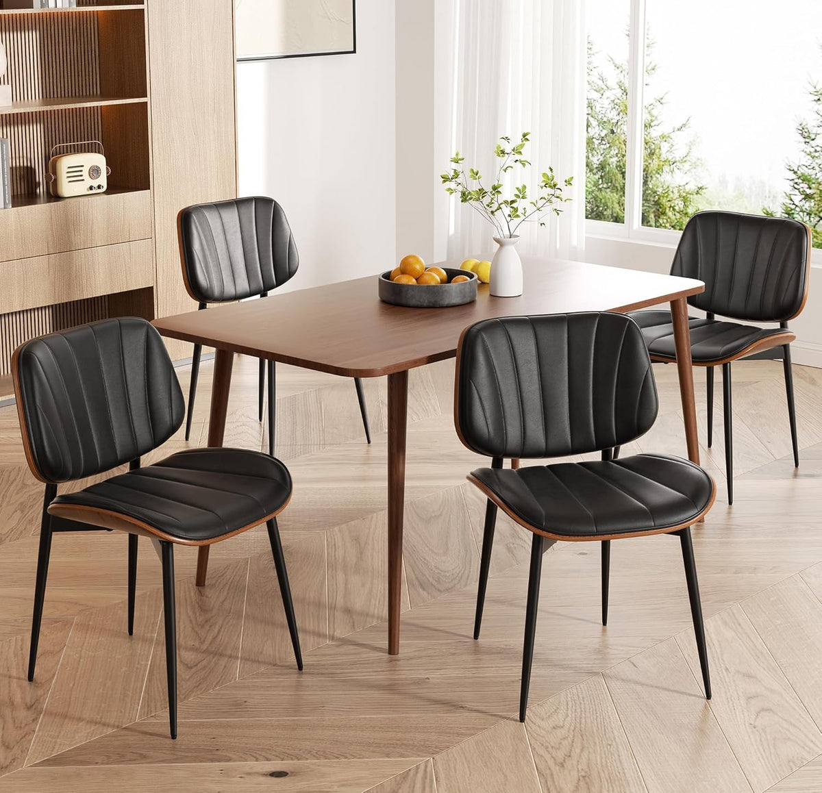 Four black faux leather dining chairs arranged around a wooden dining table in a bright dining room