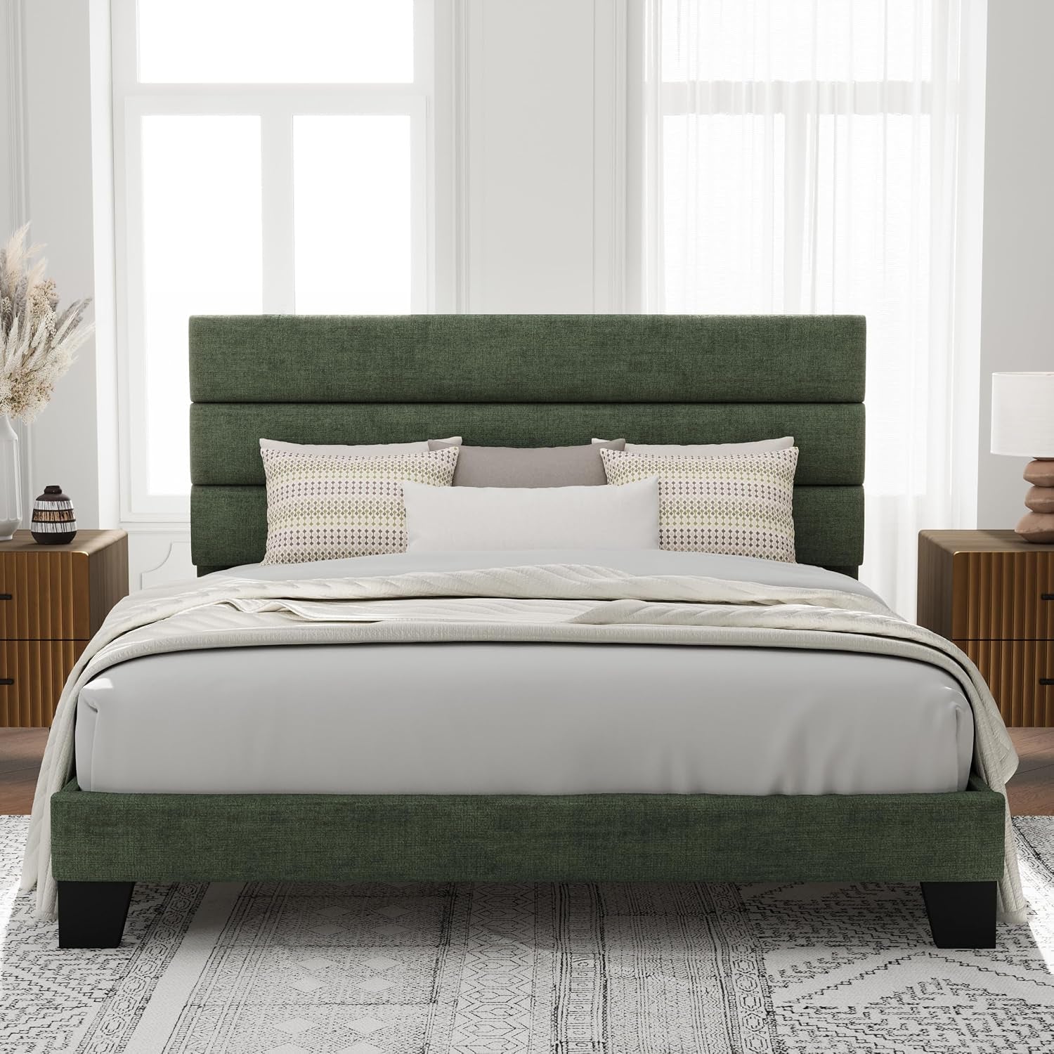 Front view of a green upholstered platform bed with layered padded headboard and dark wood legs in a styled bedroom